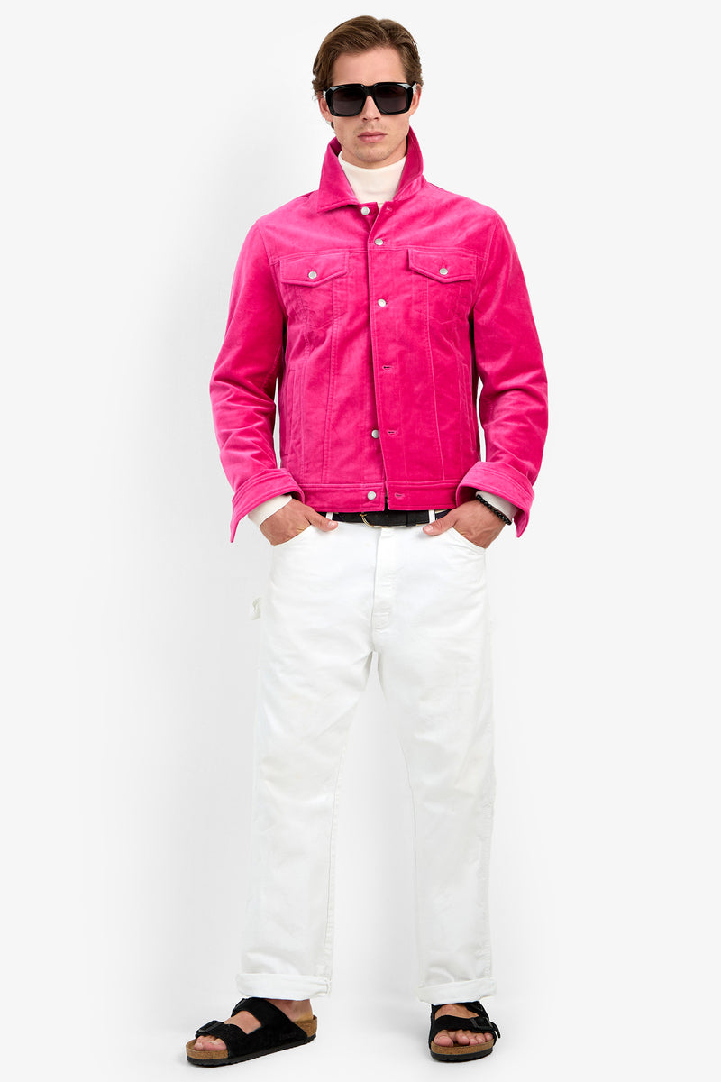 A person wearing the Angelino Trucker Jacket in TORMALINA, paired with white pants, black sandals, sunglasses, and a white shirt stands against a plain white background with their hands in their pockets.