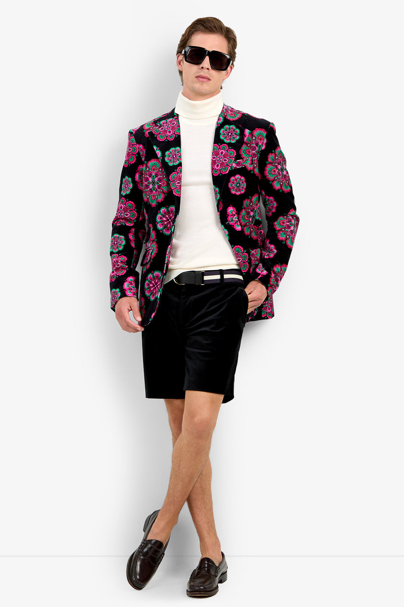 A man wearing sunglasses, a white turtleneck, the Doheny Blazer with a floral pattern, black shorts, and dark loafers stands with his legs crossed and one hand in his pocket against a plain white background.