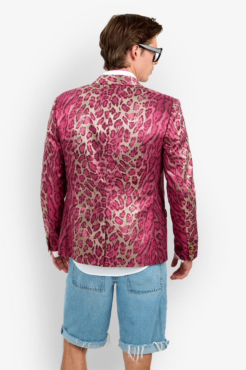 A person with brown hair wears the shiny pink leopard-print Thurston Blazer, a white shirt, jean shorts, and black glasses, facing away from the camera against a plain white background.
