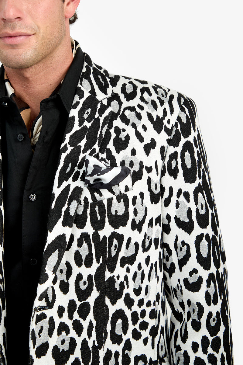 A man wearing the Thurston Blazer—a white blazer with a bold black leopard print pattern and matching pocket square—over a black shirt, with only the left half of his upper body visible.