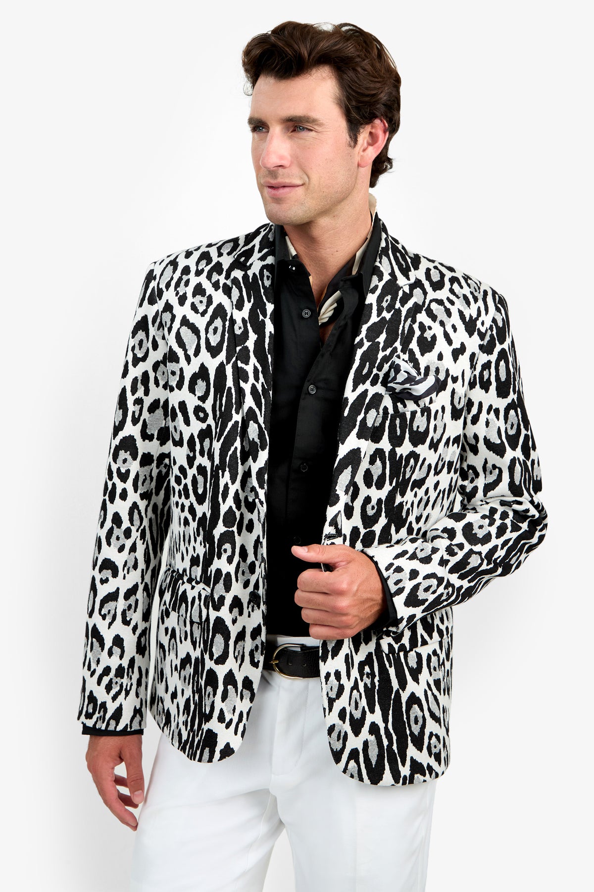 A man stands against a plain light background wearing the Thurston Blazer—a white blazer featuring a bold black leopard print pattern—paired with a black shirt and white pants.