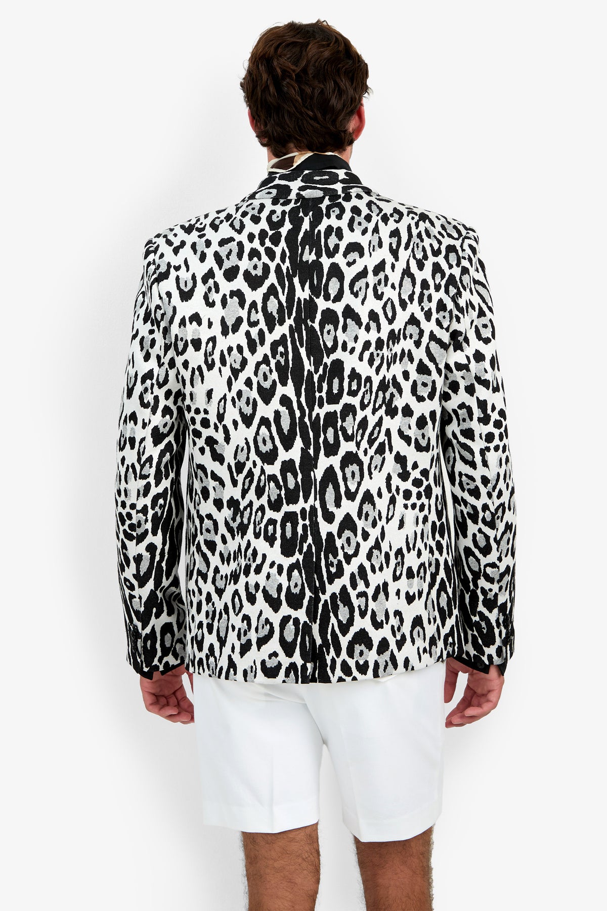 A man stands facing away, wearing the Thurston Blazer—a black and white leopard-print blazer—paired with white shorts against a plain white background.