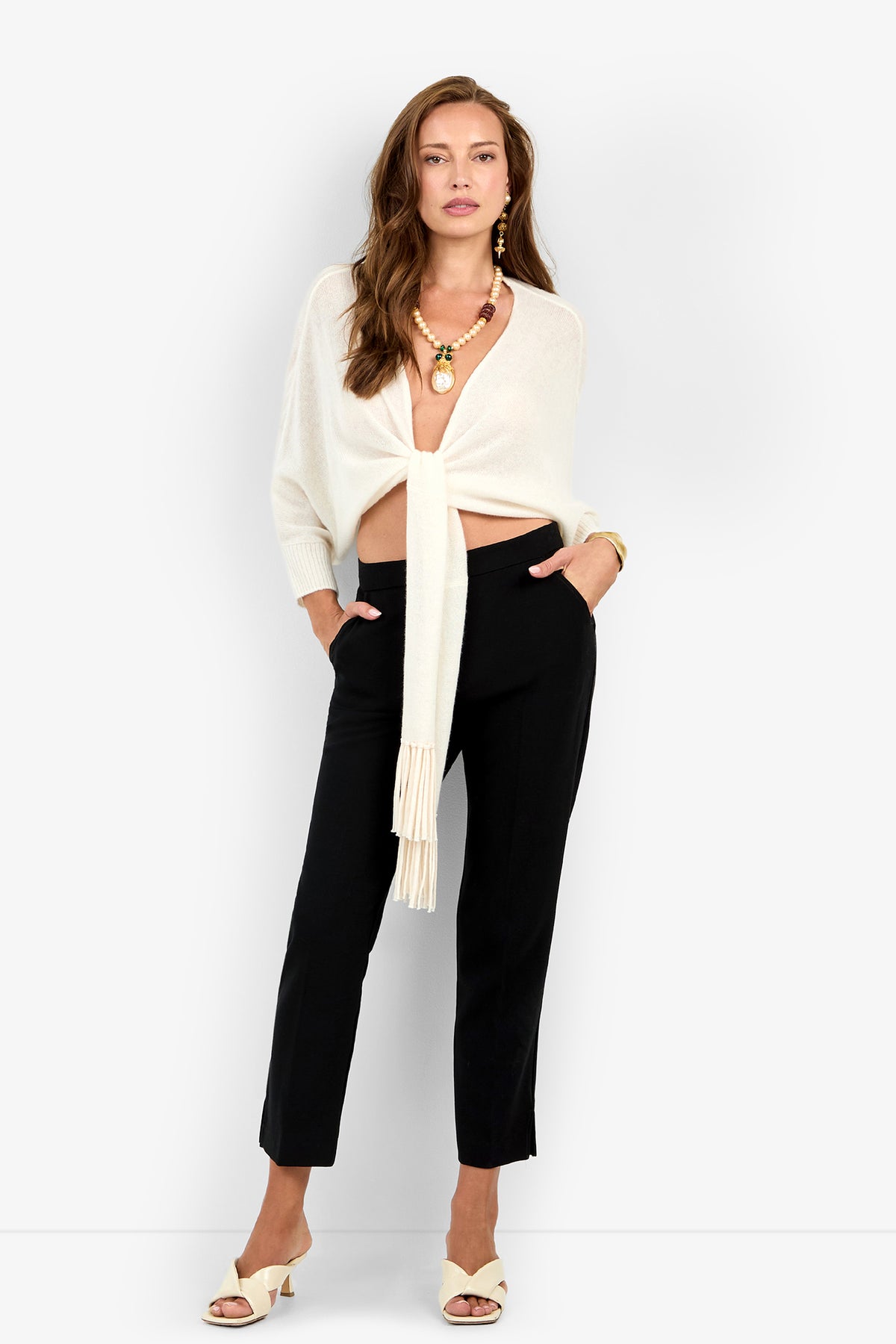 A woman wears black ankle-length ARNO PANT trousers, a cream-colored tie-front sweater, and cream mules.