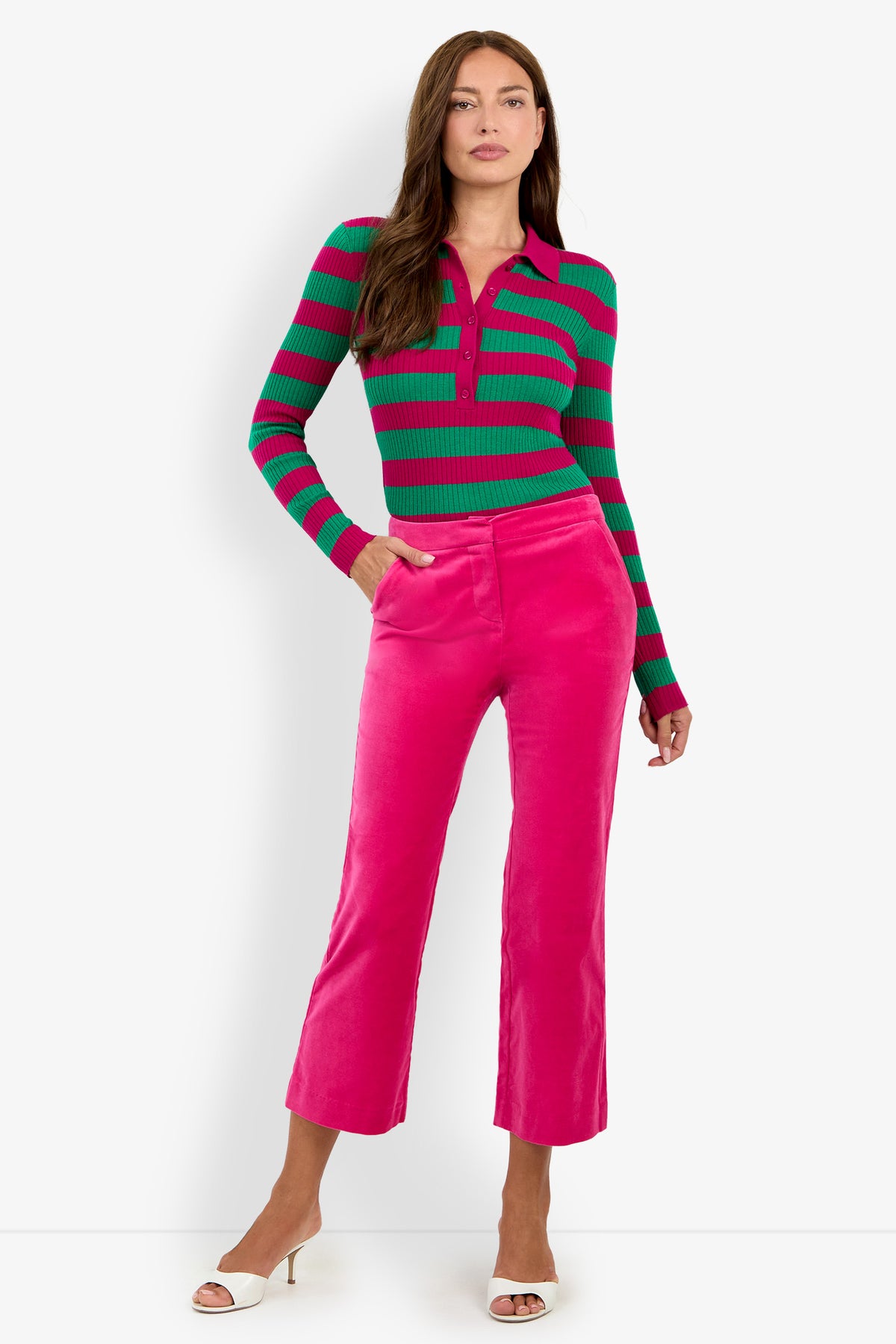 Woman standing against a white background wearing a green and pink striped long-sleeve top, the Westport Crop in bright pink, and white open-toe heels.