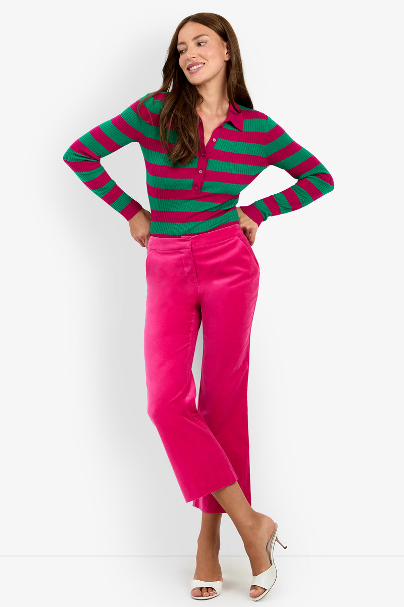 A woman smiles while wearing a green and pink striped long-sleeve top, paired with the Westport Crop pants in TORMALINA. She completes her look with white open-toe heels and stands against a plain white background.