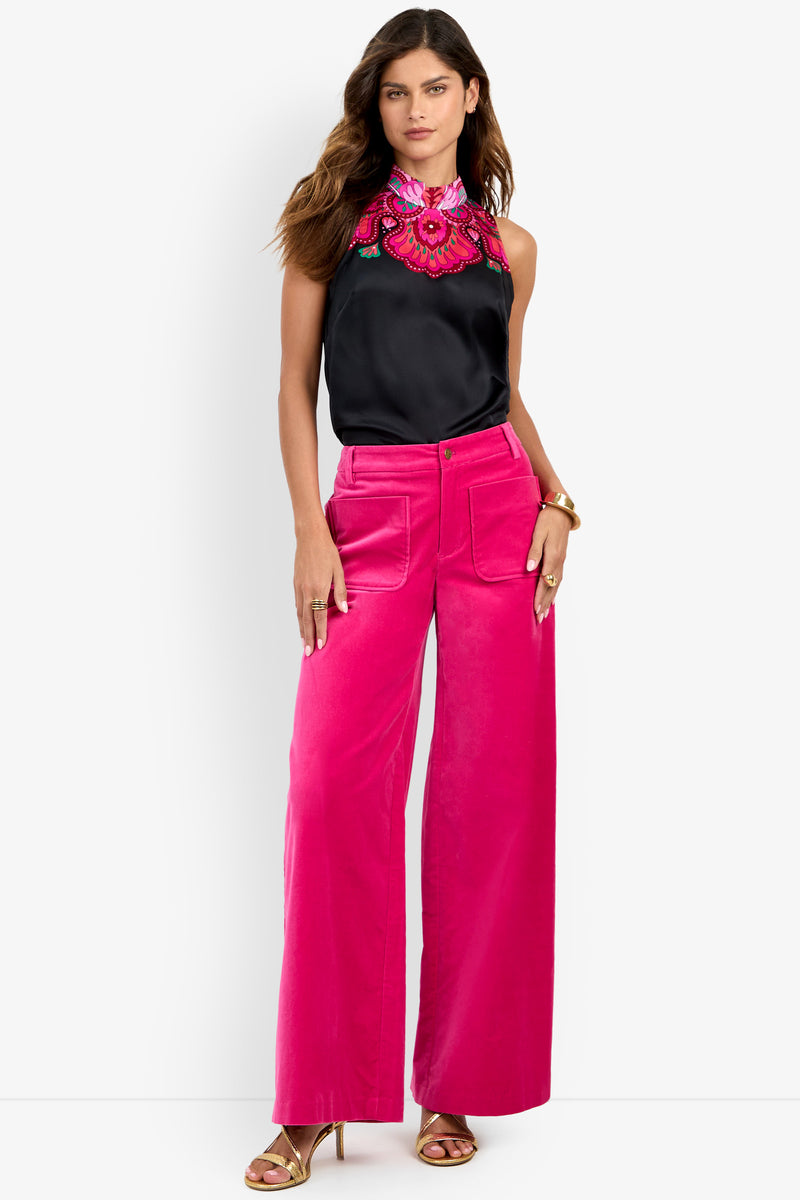 A woman wearing high-waisted, wide-leg bright pink Talamone Pant paired with a sleeveless black blouse featuring pink floral embroidery, gold sandals, and a gold bracelet.