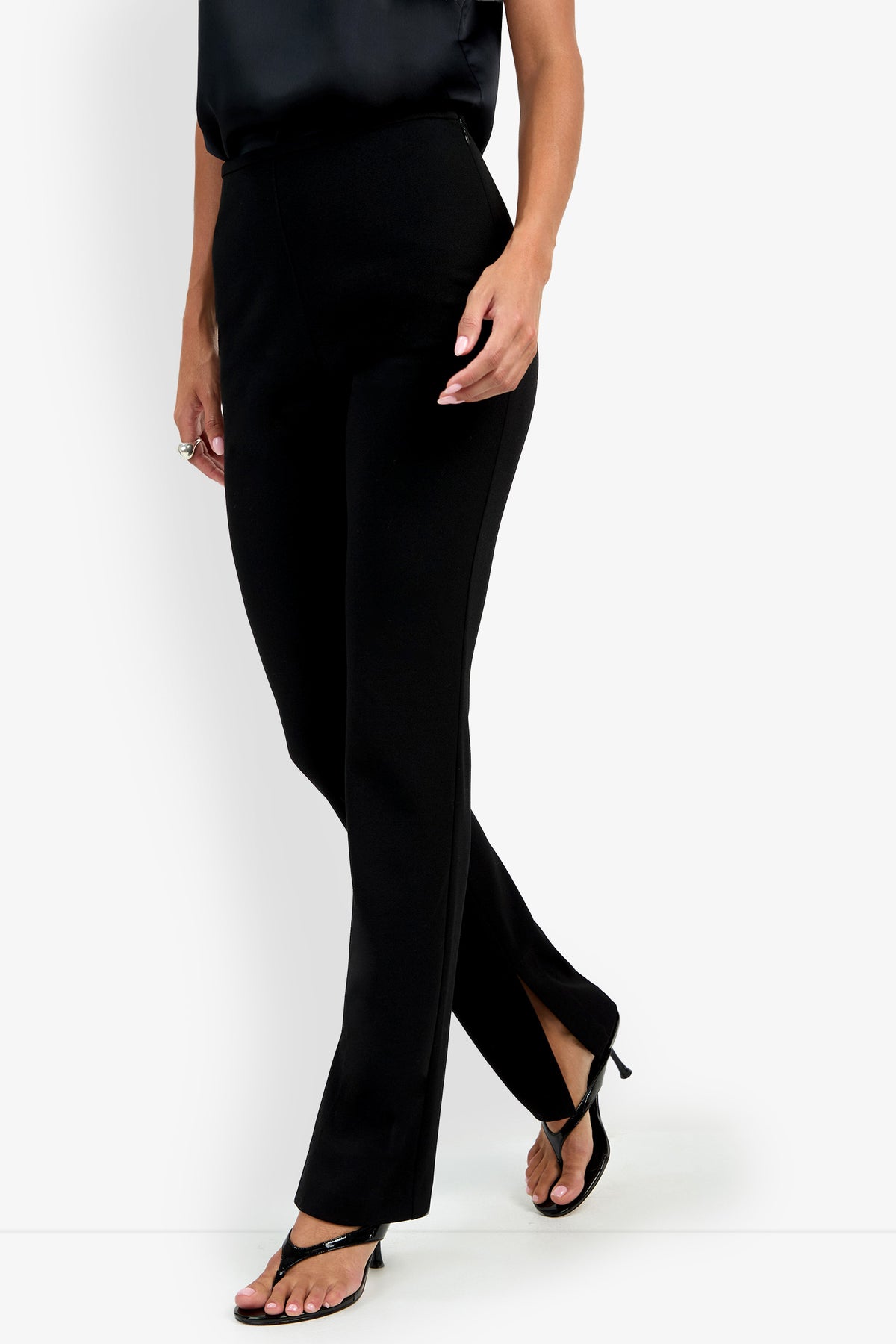 Model wearing the Milena Pant in black with black heeled sandals, shown from shoulders down against a white background.