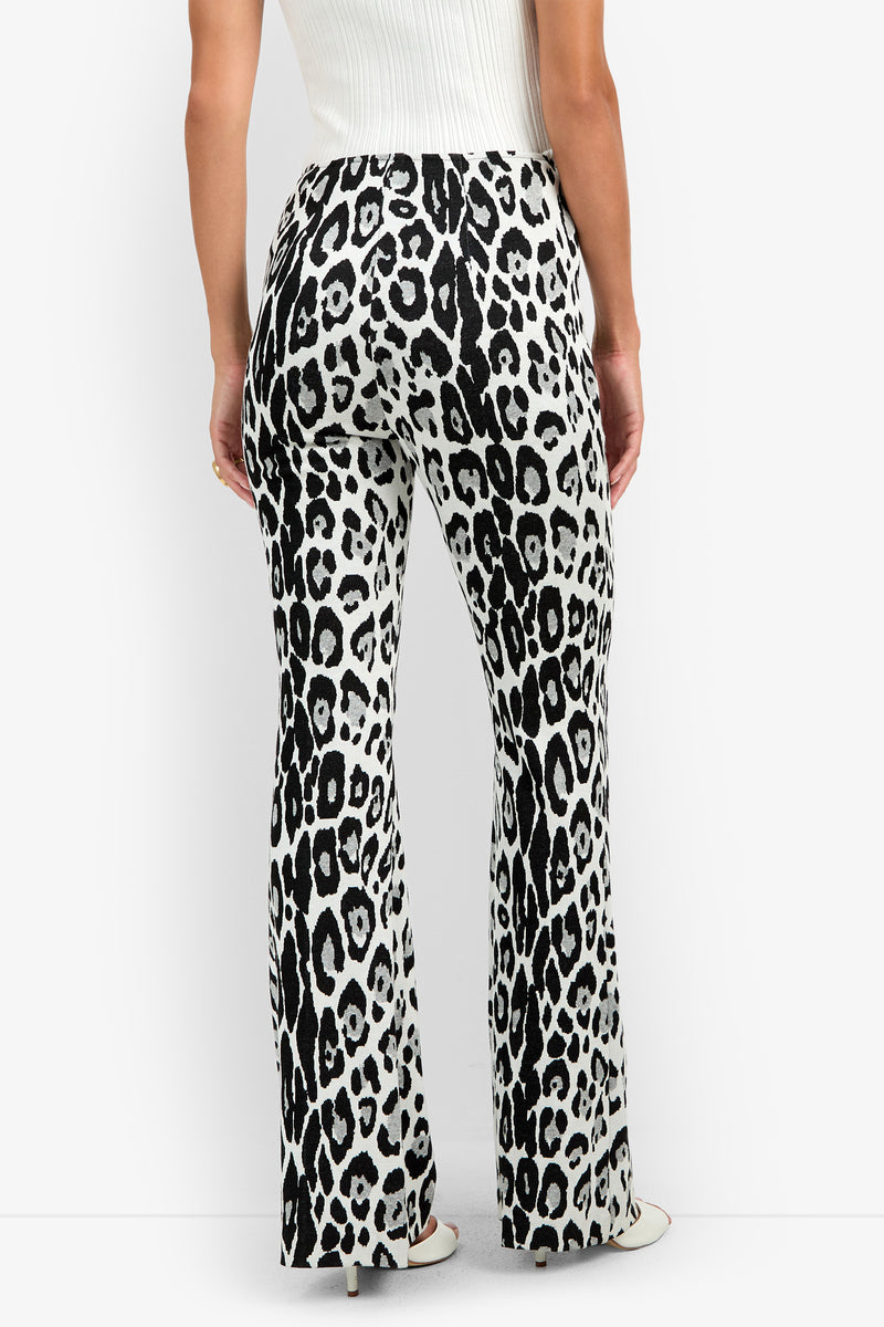 A person wearing the Jacoba Pant, featuring a high-waisted, black and white leopard print flare design, paired with a white sleeveless top and shown from the back against a plain white background.