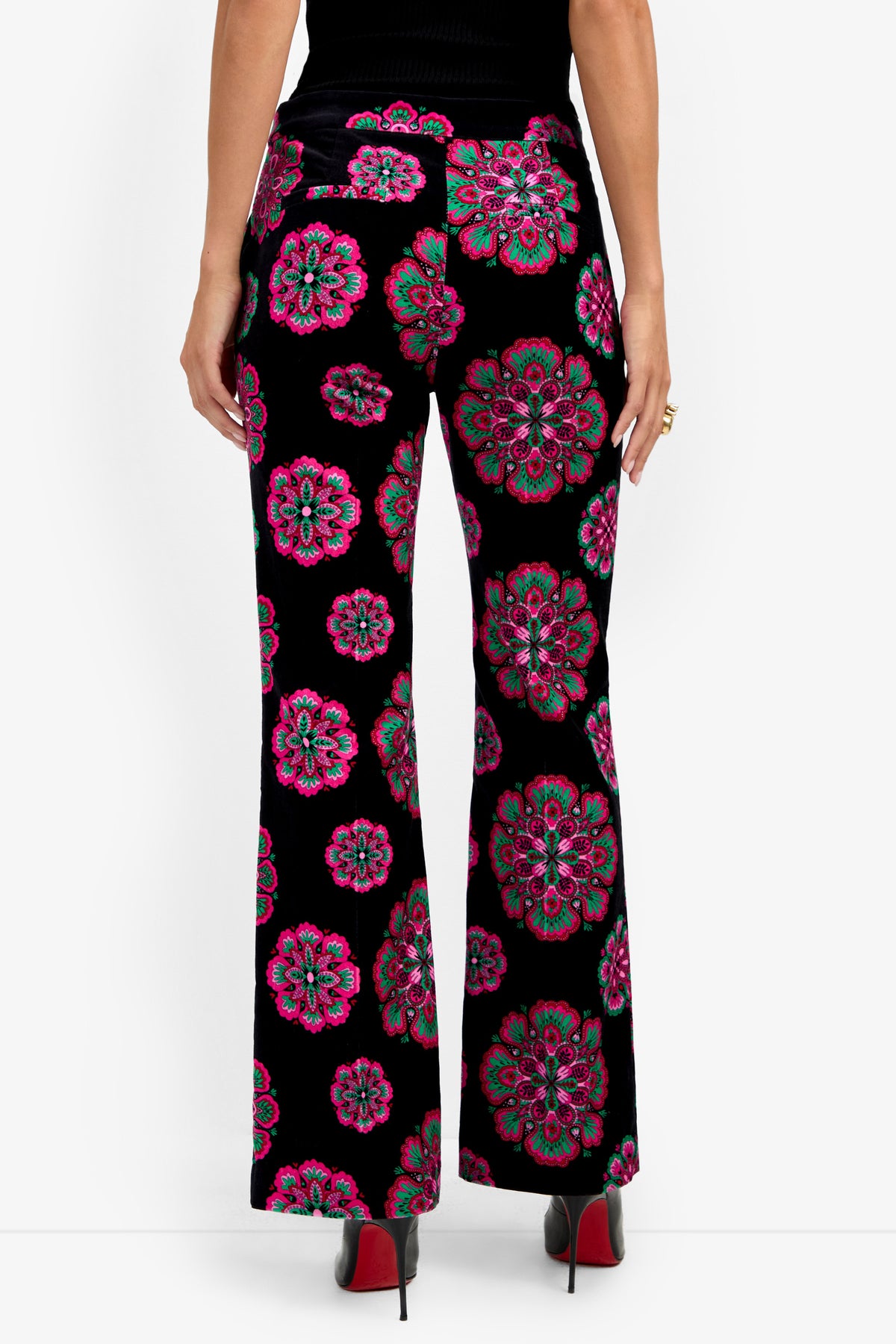 A person viewed from the back wears the Westport Pant in black, featuring bold pink, green, and blue floral patterns, paired with black high-heeled shoes.