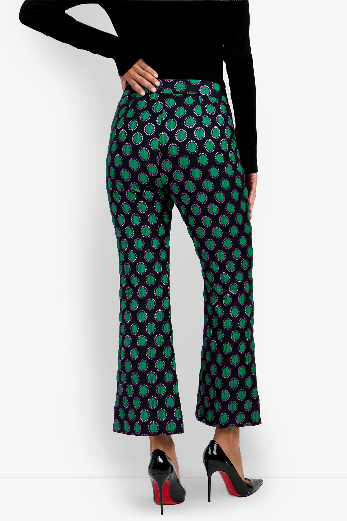 A person is seen from the back wearing the Allisan Pant, which features a vibrant green and purple geometric pattern and a flared silhouette, paired with black high heels and a black long-sleeve top.