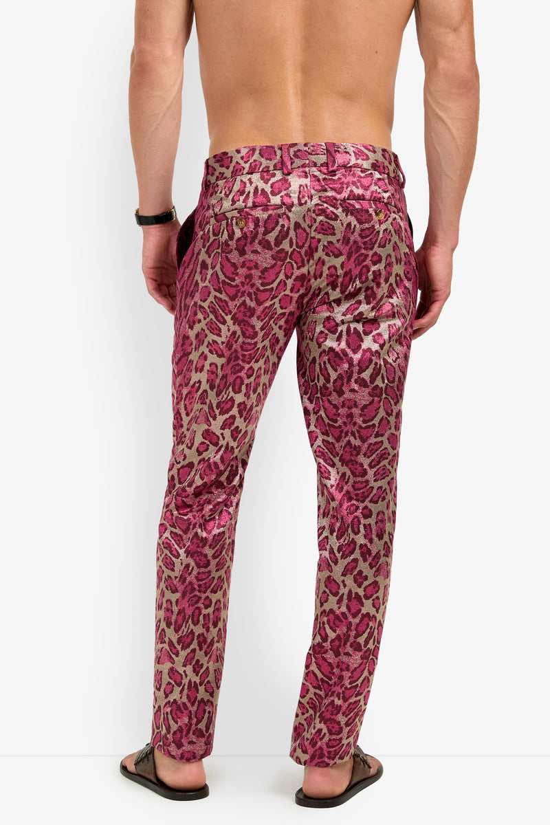 A person wearing the CLYDE SLIM TROUSER in pink and brown leopard print, paired with flip-flops, stands shirtless facing away from the camera against a white background.