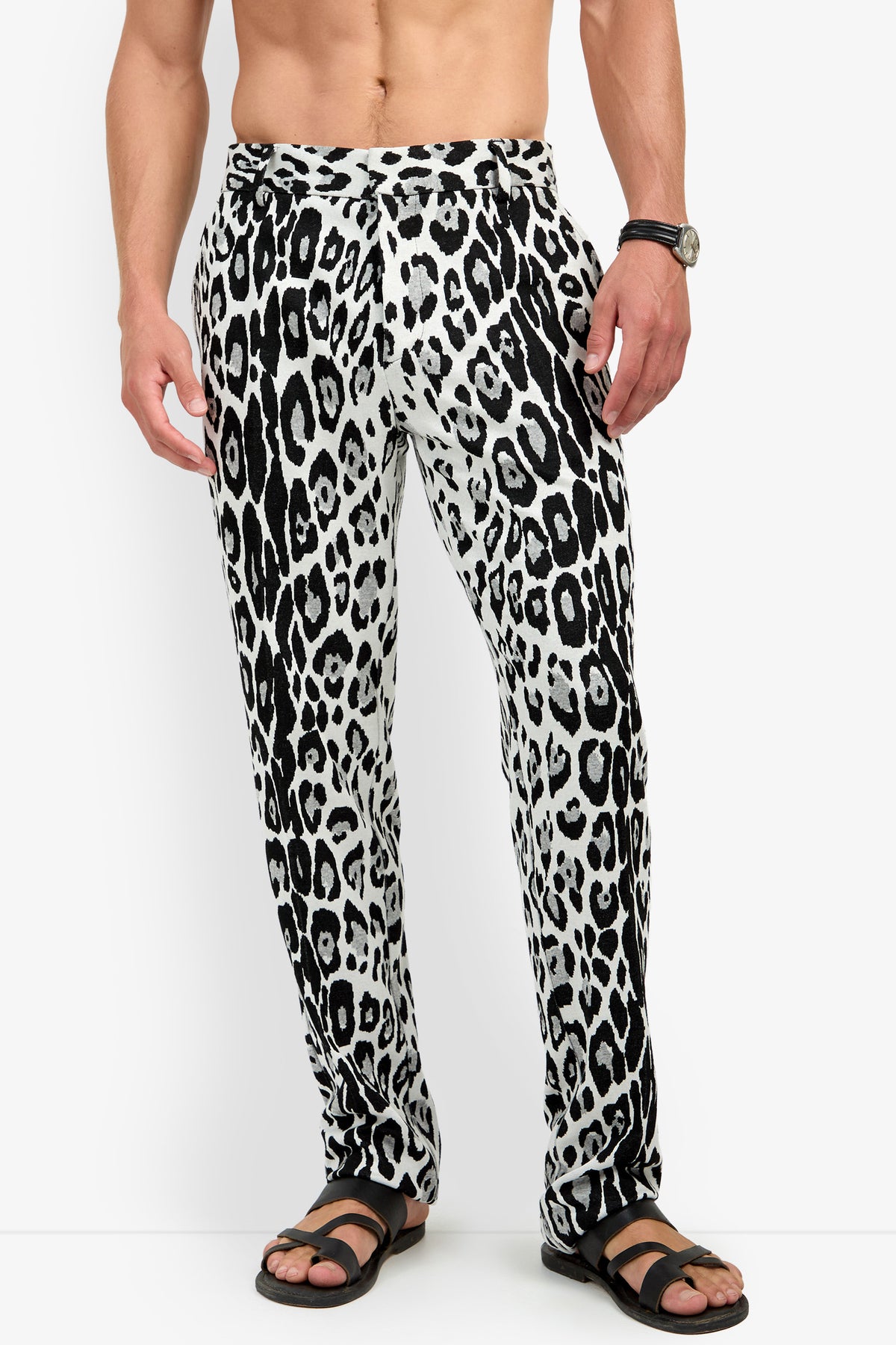 A man wearing the Clyde Slim Trouser in a black-and-white leopard print and black sandals, standing against a white background. His upper body is bare, and he has a watch on his left wrist.