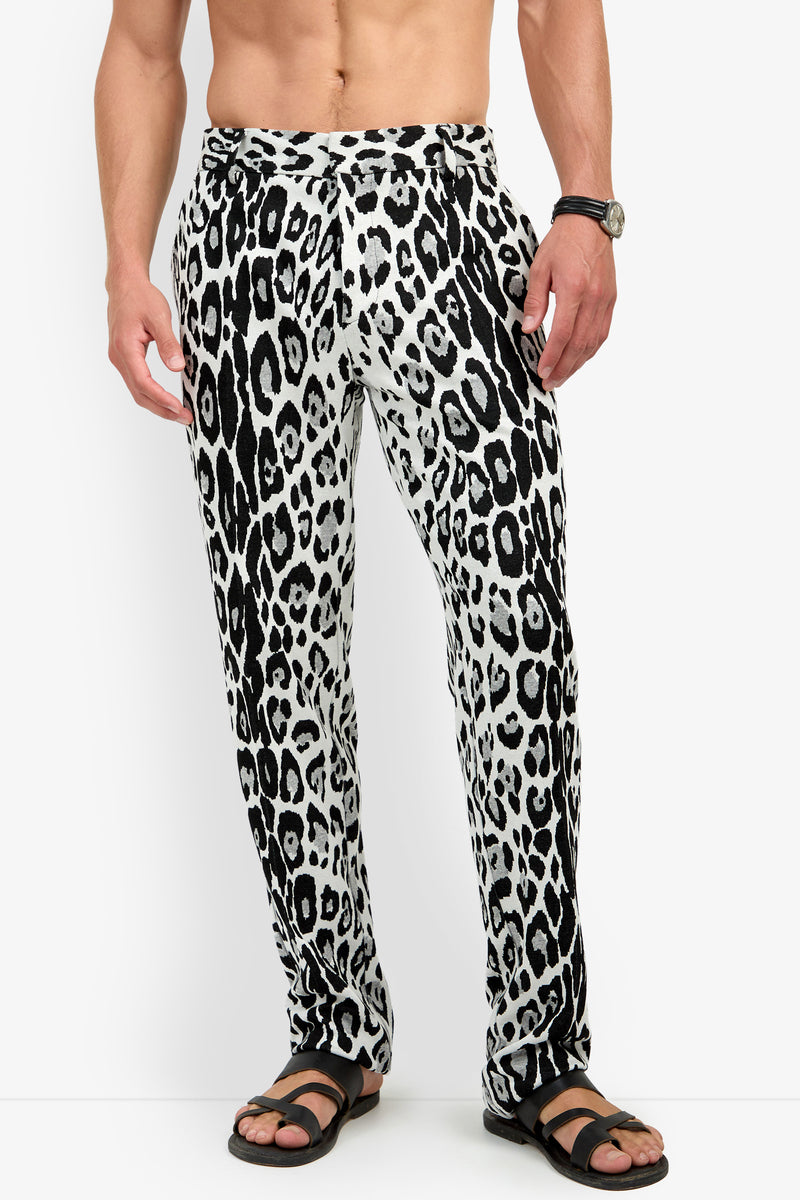 A man wearing the Clyde Slim Trouser in a black-and-white leopard print and black sandals, standing against a white background. His upper body is bare, and he has a watch on his left wrist.
