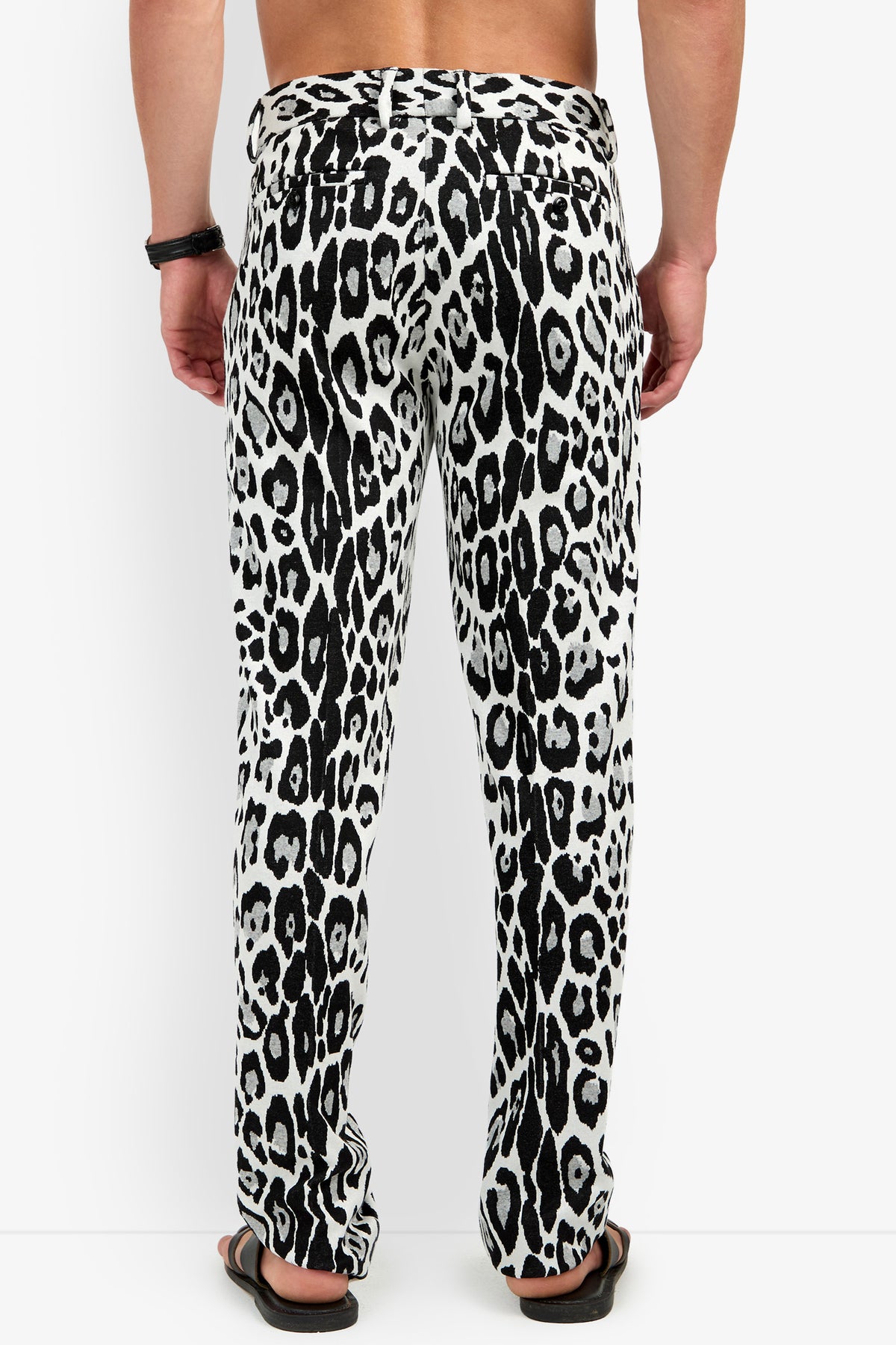 A person wearing the Clyde Slim Trouser in a black and white animal print and black sandals, shown from the back. The person is shirtless and has a black bracelet on their right wrist.