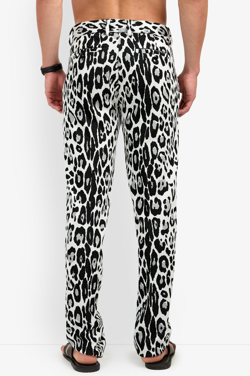 A person wearing the Clyde Slim Trouser in a black and white animal print and black sandals, shown from the back. The person is shirtless and has a black bracelet on their right wrist.
