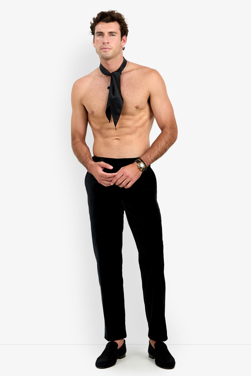 A shirtless man wearing the Clyde Slim Trouser, black loafers, a wristwatch, and a loose black necktie stands against a plain white background.