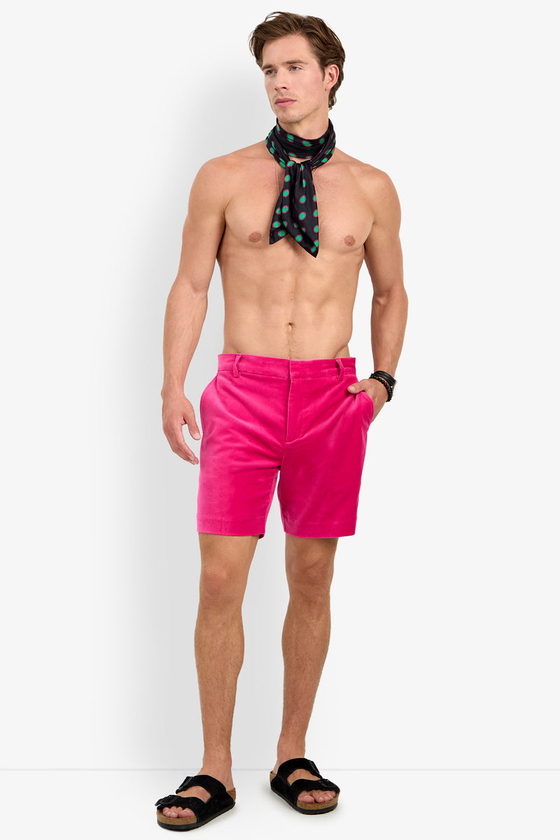 A man stands shirtless against a plain white background, wearing LAWRENCE SHORT in bright pink, black sandals, a black polka dot scarf around his neck, and a watch on his left wrist.
