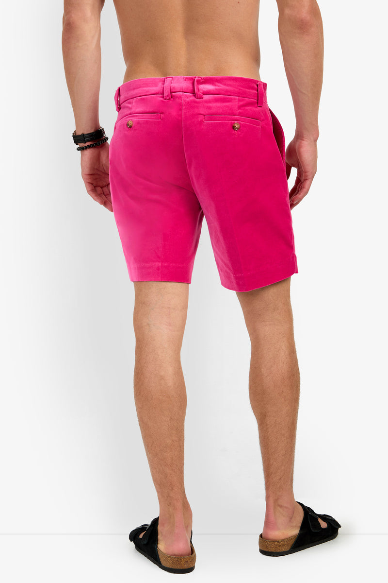 A shirtless person seen from behind wearing the LAWRENCE SHORT in bright pink, along with black bracelets and black sandals, standing against a plain white background.