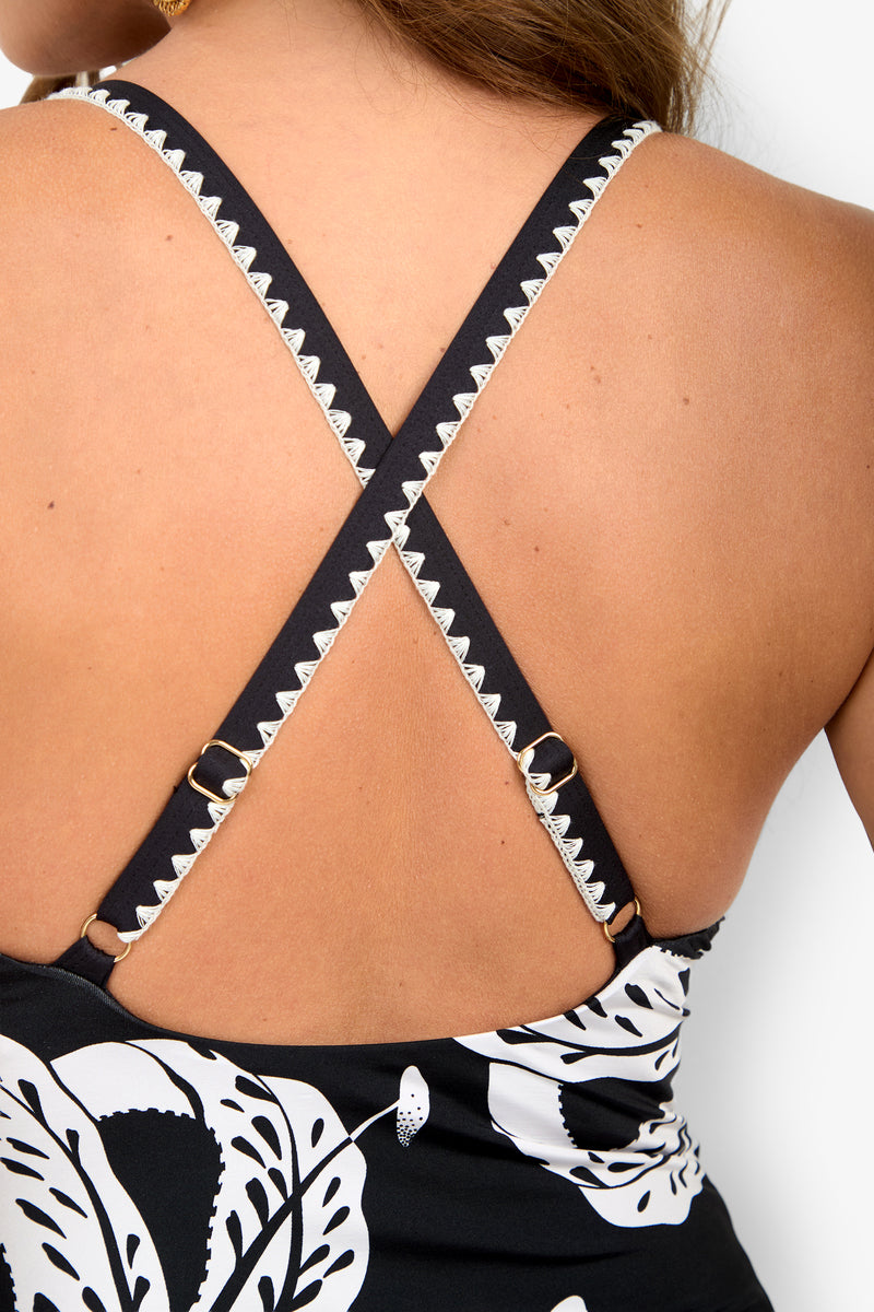 A black and white patterned GOLDEN HOUR BLOOM BALCONETTE MAILLOT one-piece swimsuit with crisscross back straps, white embroidered trim, and gold metal hardware.