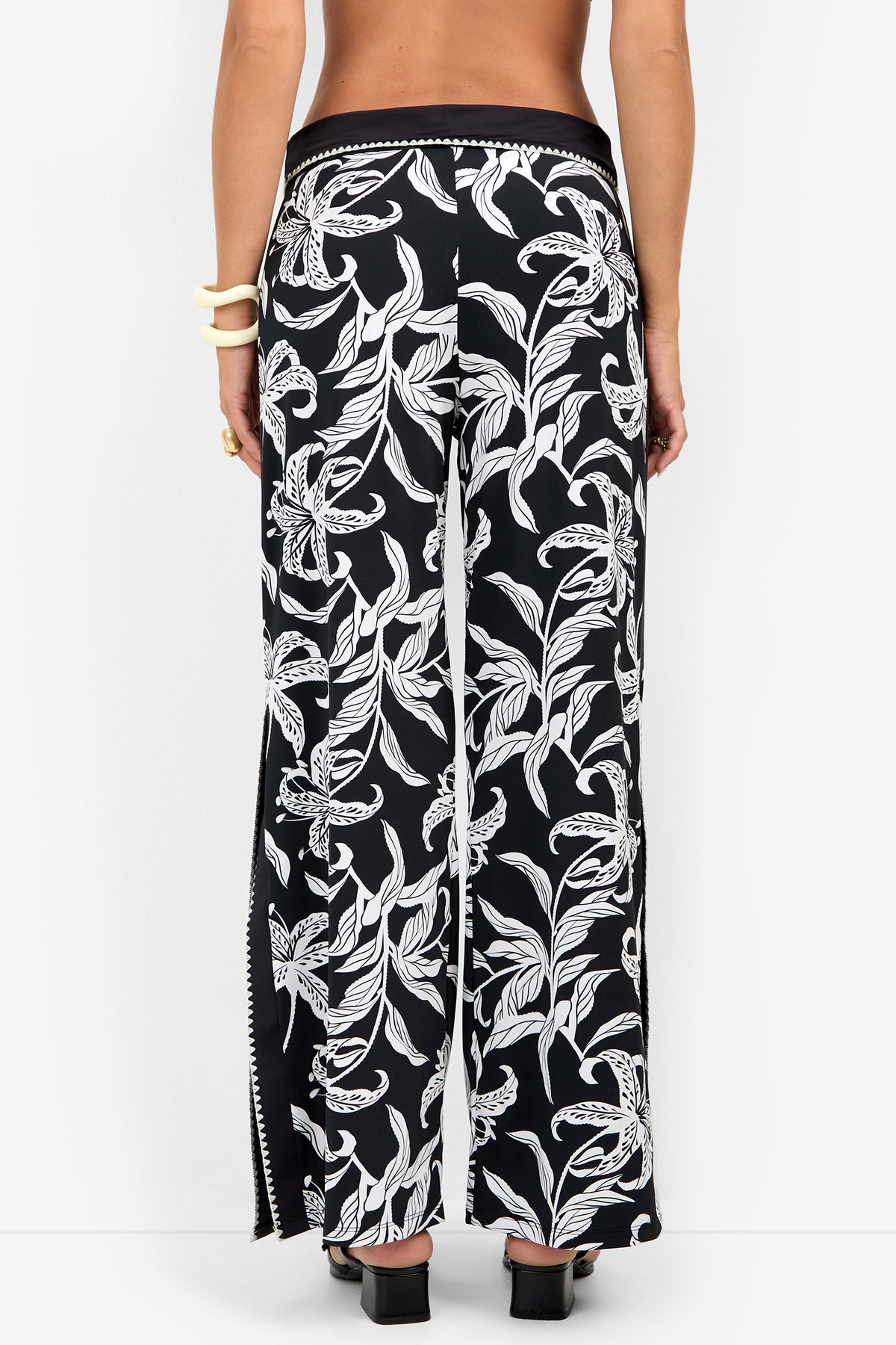 Back view of GOLDEN HOUR BLOOM SWIM PANT, featuring high-waisted, wide-leg floral swim pants in a black and white pattern with side slits.