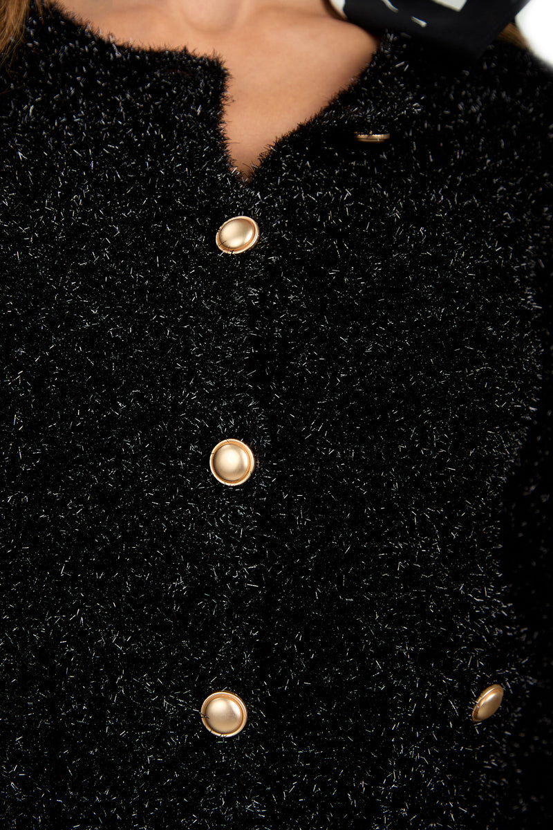 Close-up of a person wearing the Sinai Cardigan, a textured black fuzzy jacket with shiny gold buttons, and a small part of a black and white patterned scarf visible at the neckline.