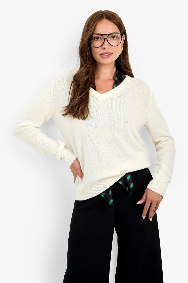 A woman wearing the cream EVANGELINE SWEATER in 100% cashmere over a patterned collared shirt and black trousers.