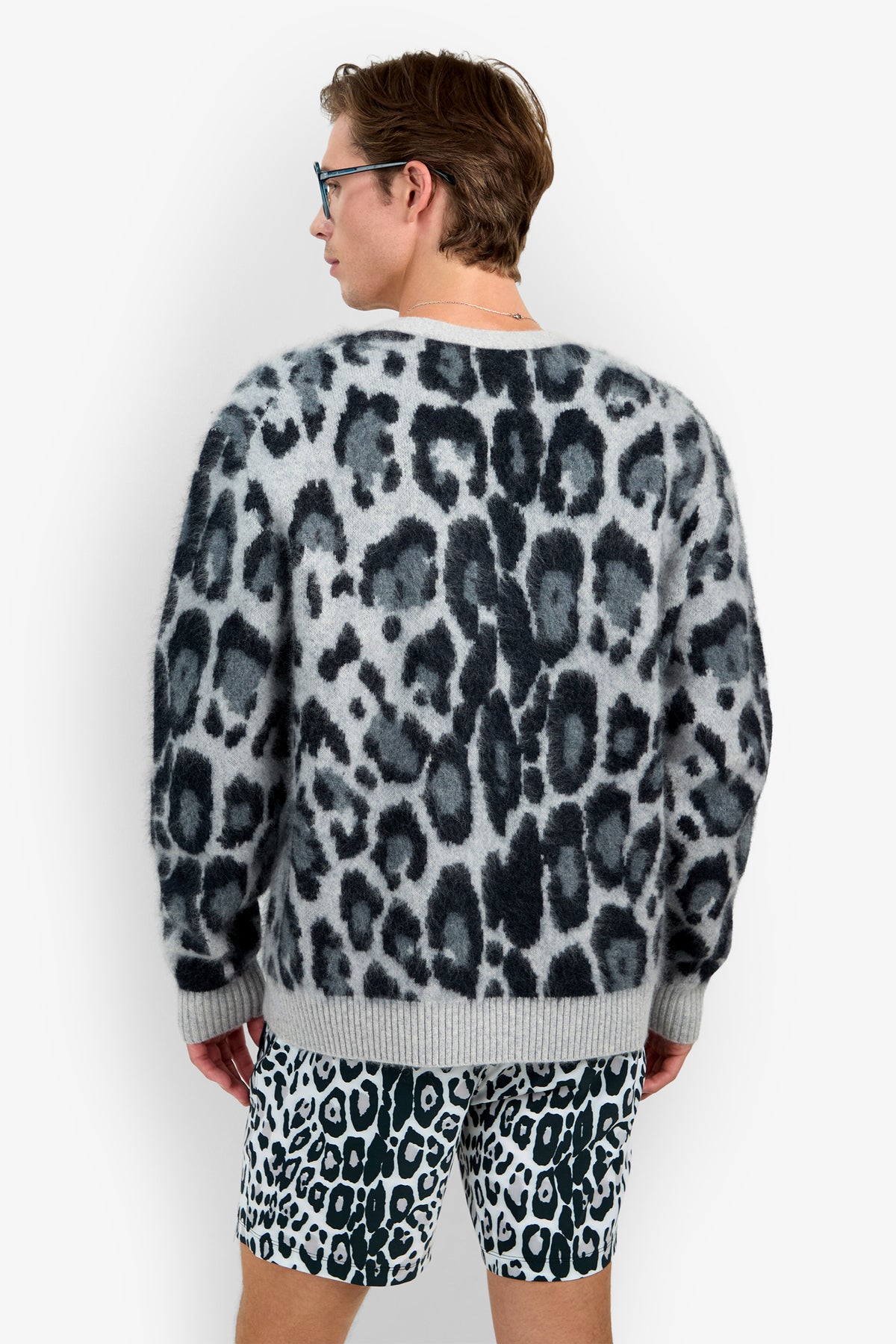 Wearing the LEO FUZZY CARDIGAN, a person faces away from the camera, pairing it with black-and-white leopard print shorts while standing against a plain white background.