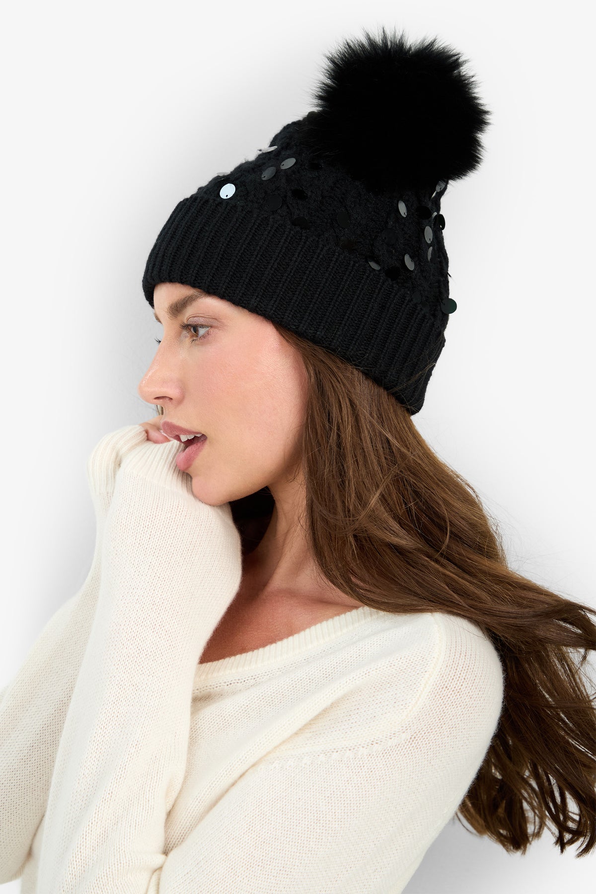 A woman wears the DALIDA SEQ. HAT, a black sequined beanie made of 100% wool, topped with a black pom-pom.
