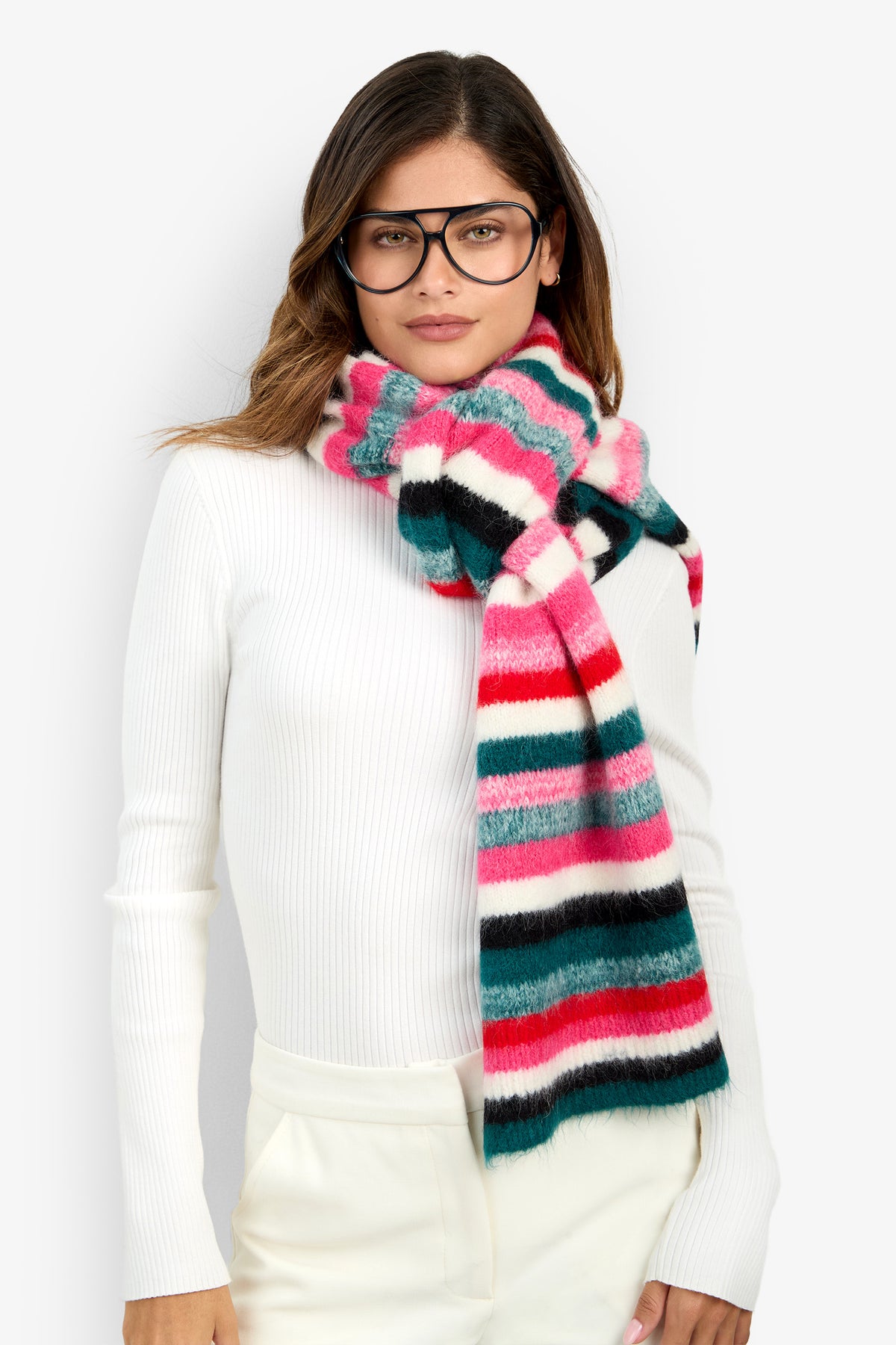 A person wearing black-framed glasses and a multicolored CARDUCCI STRIPE SCARF in shades of pink, red, teal, and black, paired with alpaca socks.