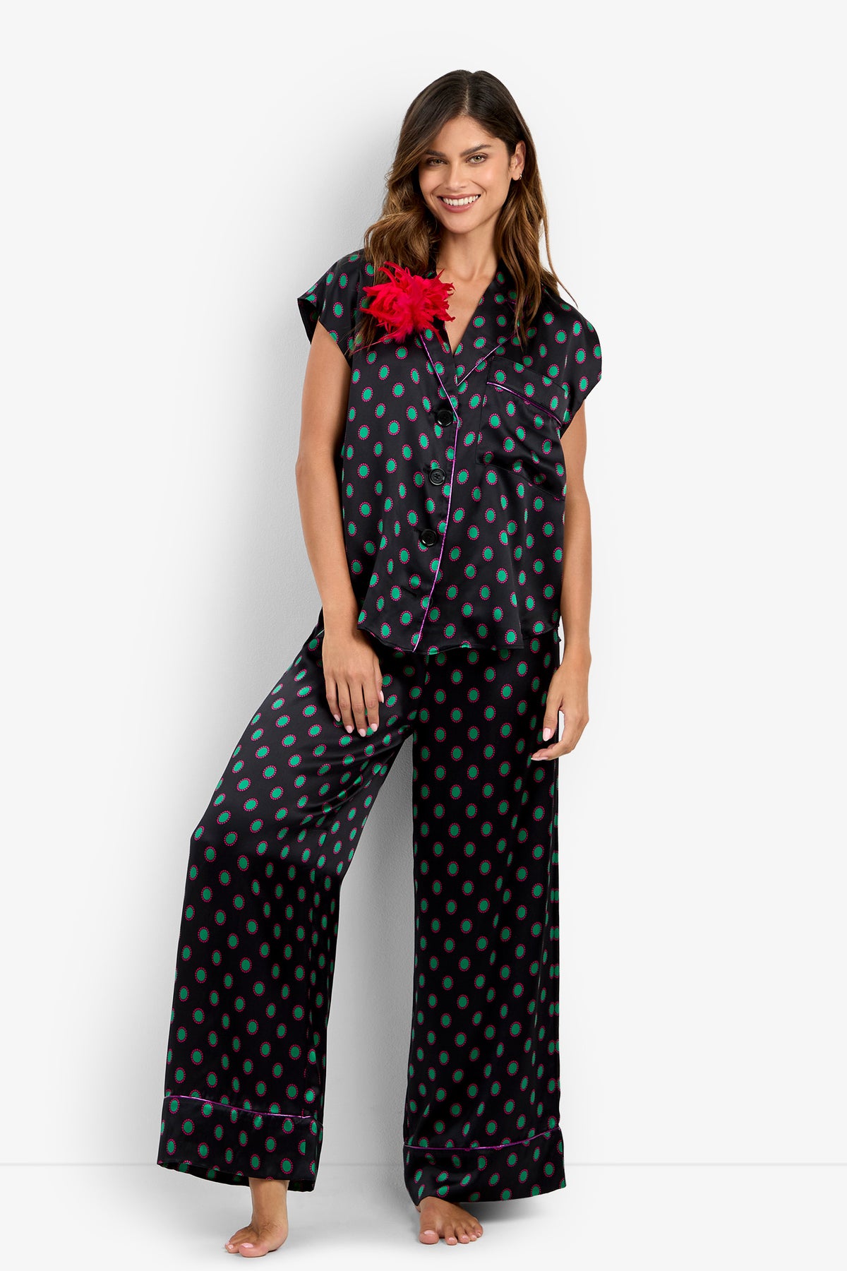 A woman wears the ADARA 2 TOP in black silk with green polka dots, purple piping, and a large red flower on the collar, paired with matching wide-leg pants.