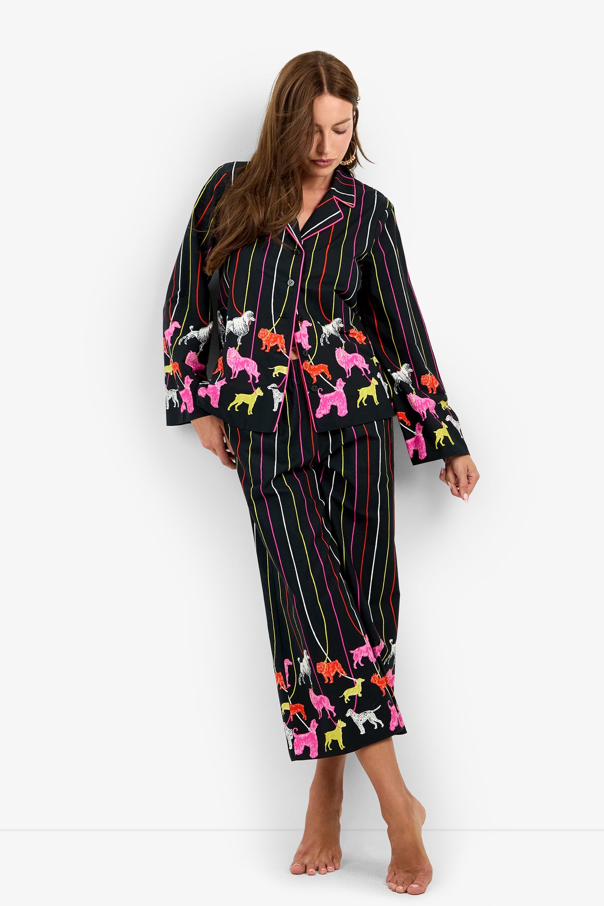 A person wearing a RUBEE PANT set in black with vertical multi-colored stripes and a pattern of brightly colored dogs along the cuffs and hem.
