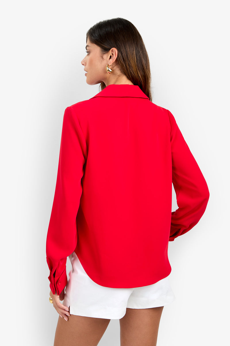 A woman seen from the back wearing a long-sleeved, bright red polyester MISTIC TOP and white shorts.