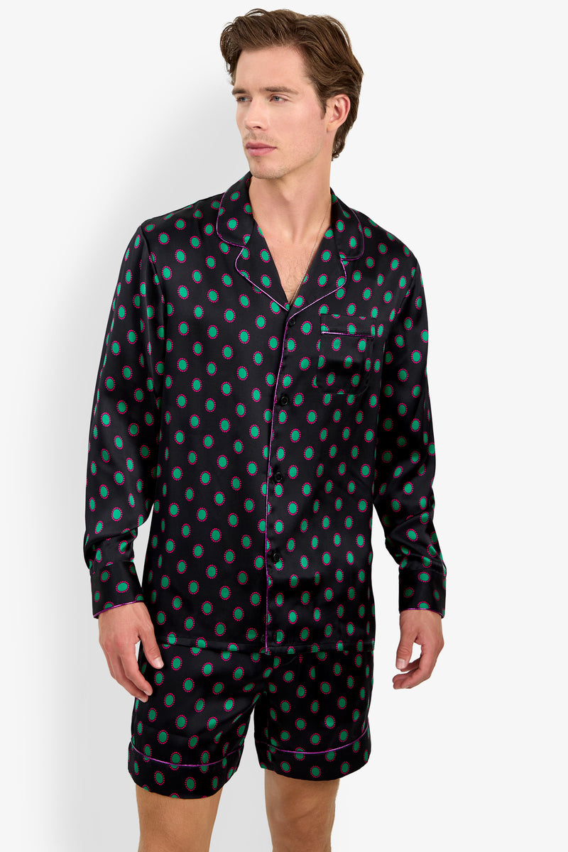 A man wearing a black PJ TOP in 100% silk with long sleeves and matching shorts, both featuring a green and pink circular pattern.
