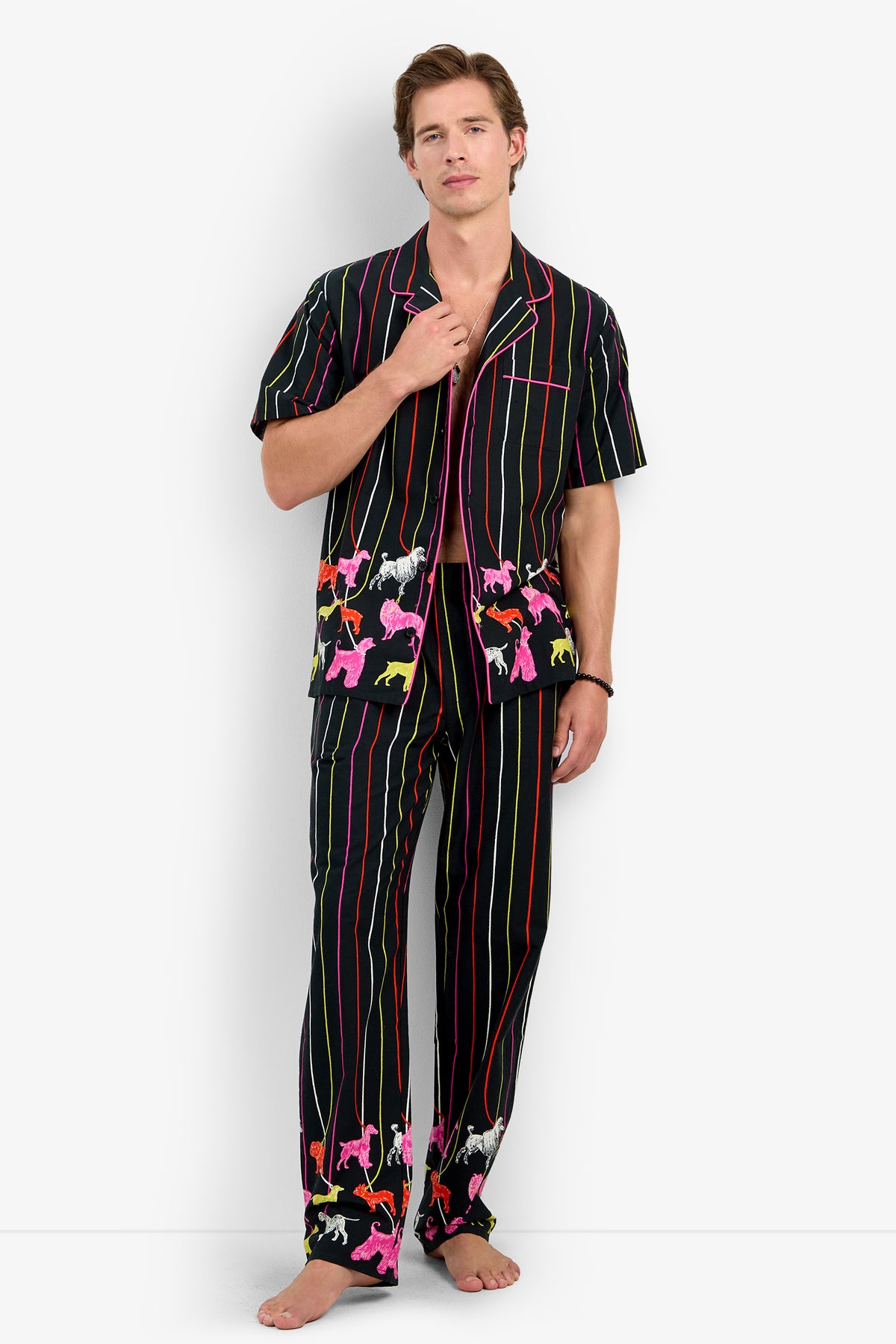 A man wears a 100% cotton PJ TOP with matching pants, featuring vertical neon stripes and a colorful pattern of small poodles.