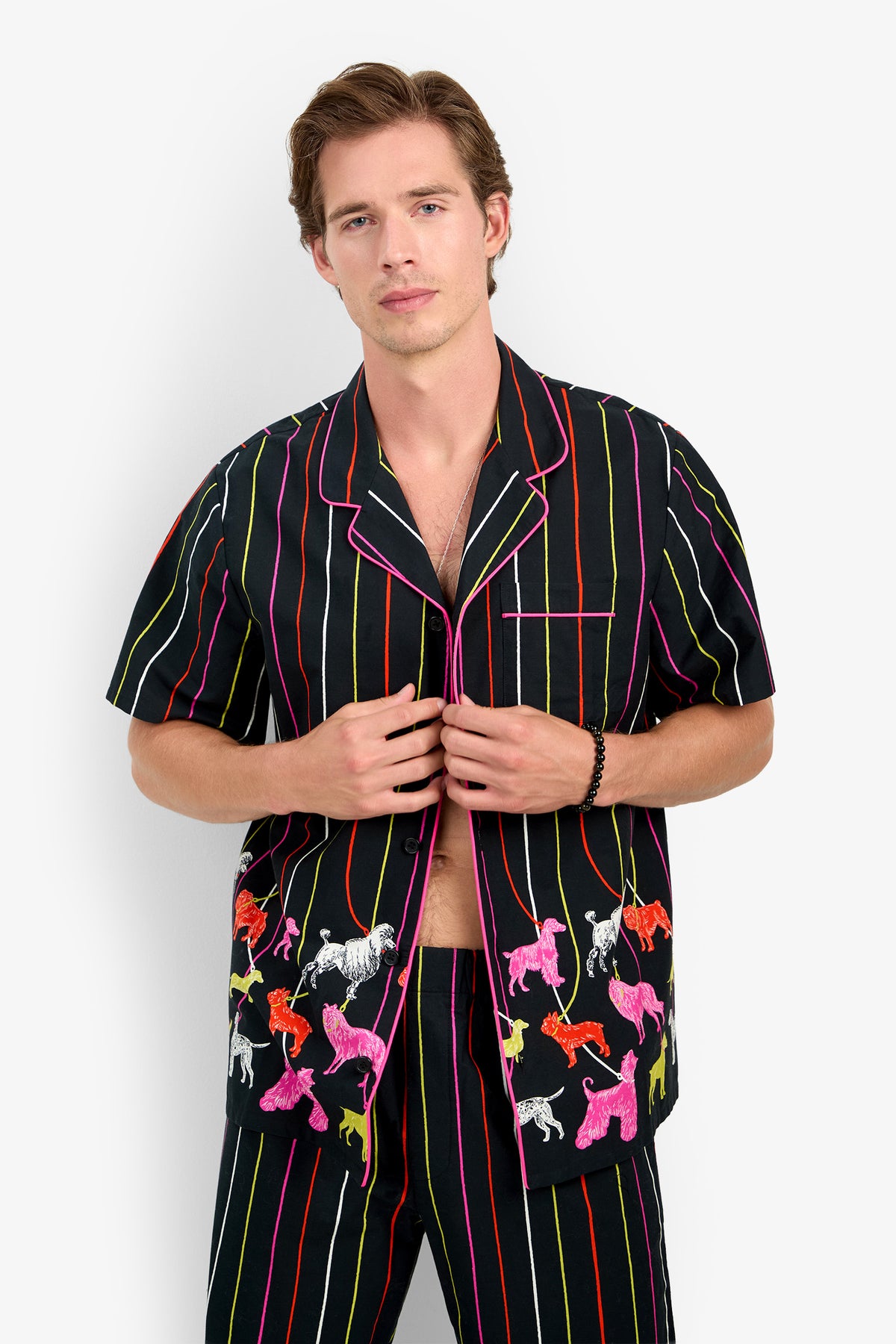 A man wears a PJ TOP made of 100% cotton with short sleeves, vertical stripes, and a colorful poodle print.