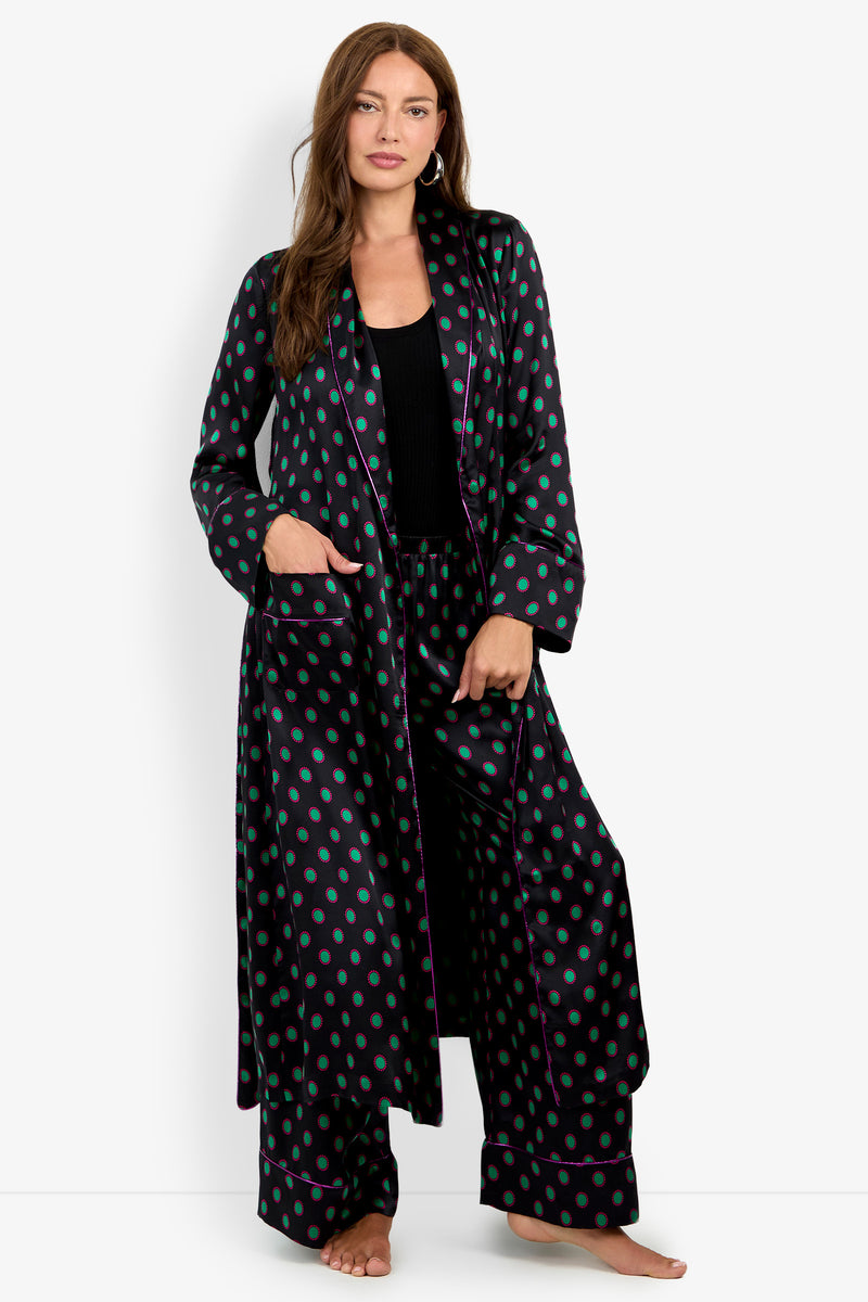 A person wearing an ADALYNN ROBE, a long, black silk robe with a green polka dot pattern and purple trim, over matching wide-leg trousers.