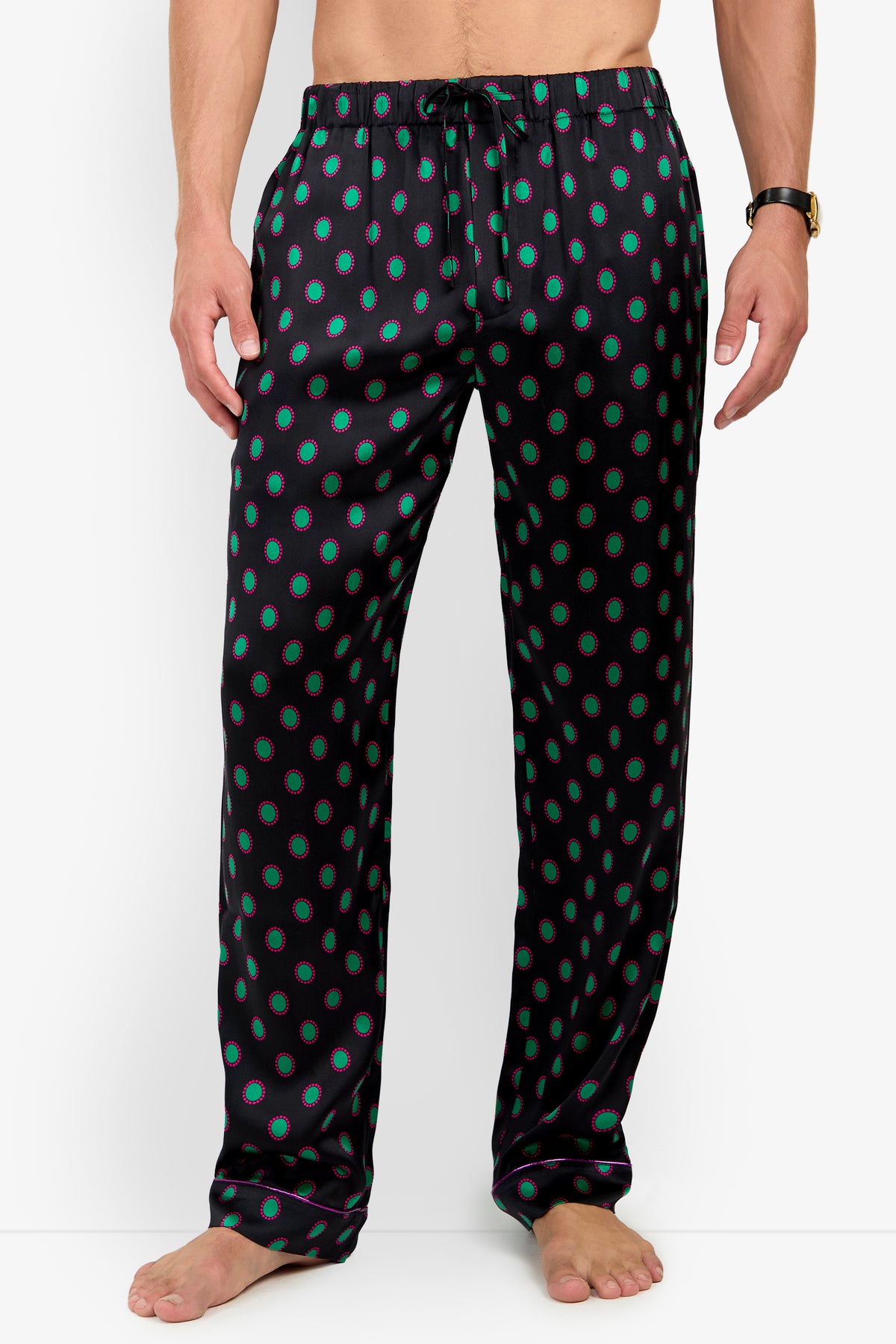 A person wearing PJ PANT silk pajama pants with a repeating pattern of green ovals outlined in pink and a drawstring waistband.