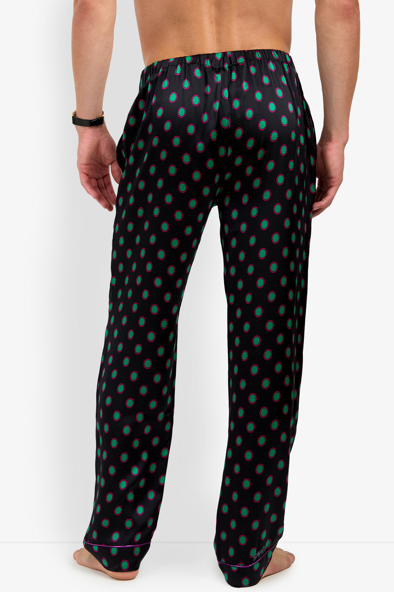 Back view of a person wearing black PJ PANT 100% silk pajama pants featuring a repeating pattern of green circles outlined in pink.