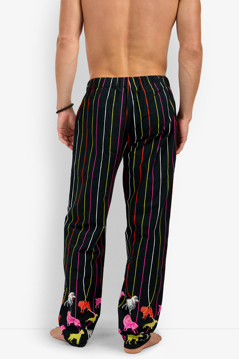 A person seen from behind wearing PJ PANT, 100% cotton pajama pants featuring vertical neon stripes and colorful dog motifs at the cuffs.