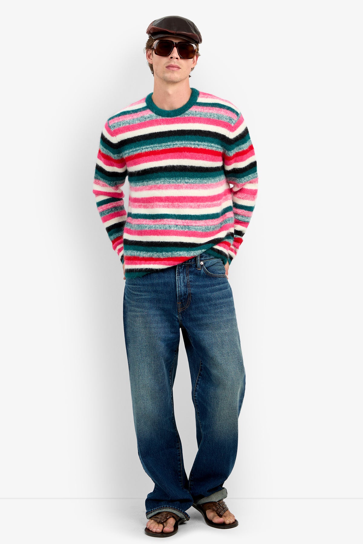 A person wearing the MR. BARDINI pink, white, and teal striped wool sweater, blue jeans, sunglasses, and a flat cap.