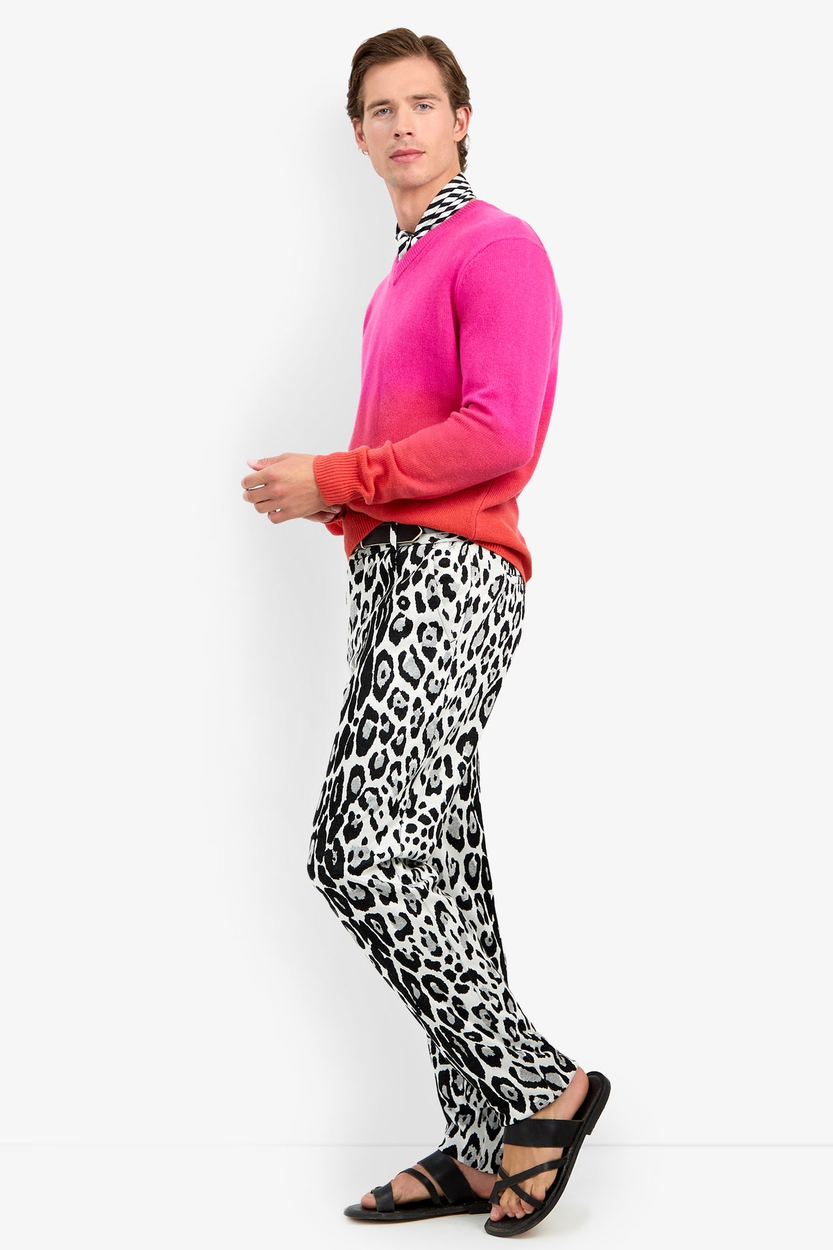 A man wearing a TIMOTHY OMBRE pink and orange sweater over a black and white striped shirt, styled with leopard print trousers and black leather sandals.