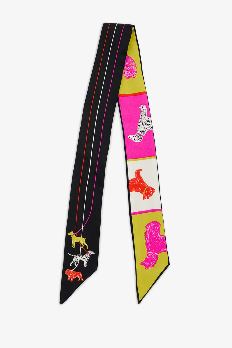 The POOCH TWILLIE SCARF is a long, narrow 100% silk scarf with one black side featuring three dogs on leashes and the other side featuring a series of pink, white, and yellow rectangular panels, each containing a dog illustration.