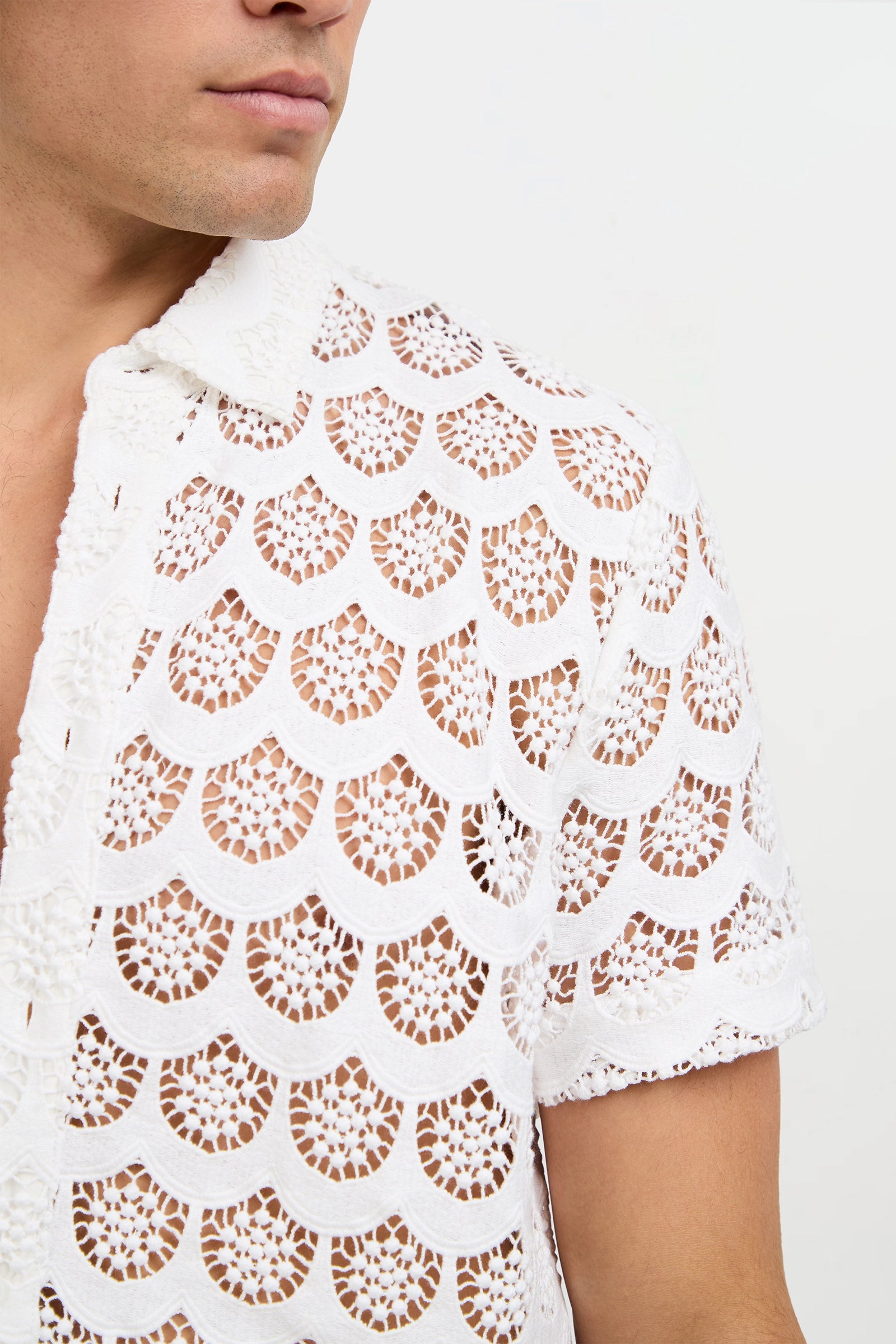 A man wears the Branson Crochet Lace Shirt—a white, short-sleeve, semi-transparent shirt with an intricate scallop-shaped lace pattern. Only the lower part of his face and upper torso are visible.