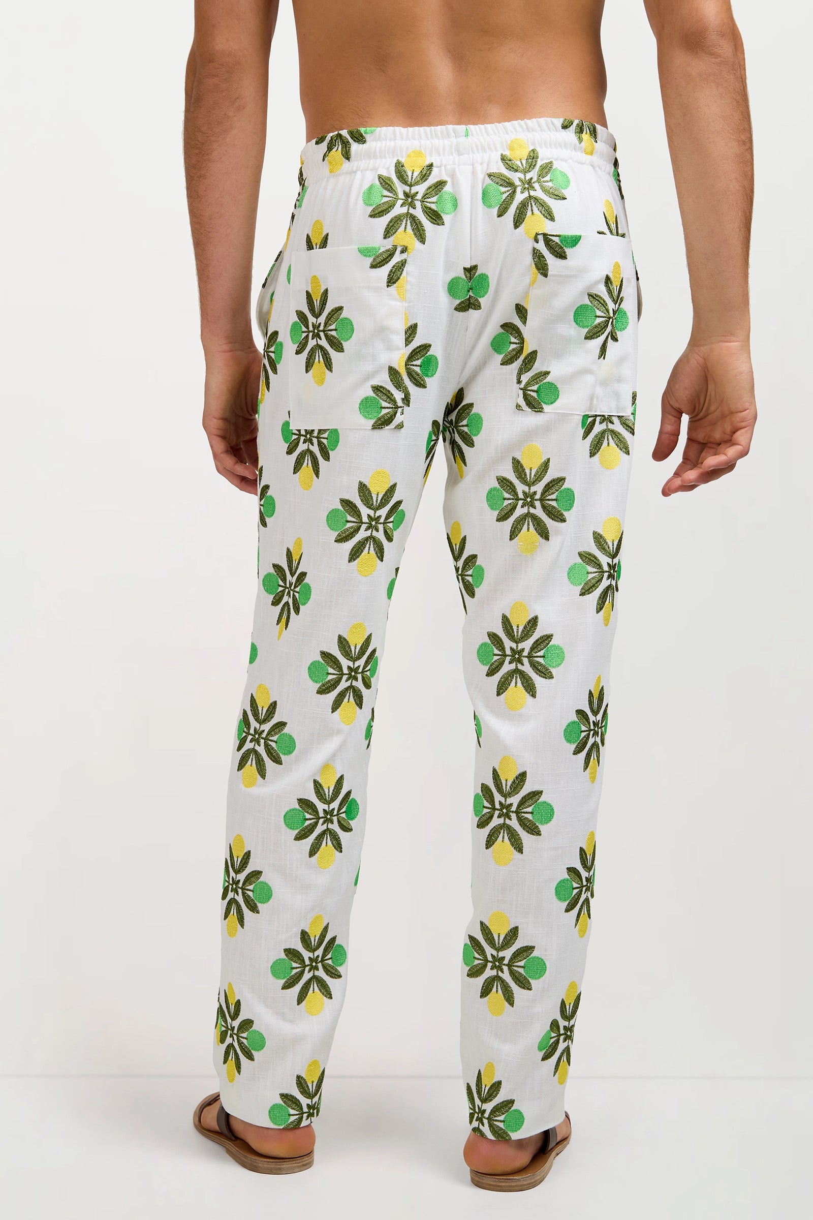 A man is seen from the back, barefoot against a plain background, wearing the Felipe Drawstring Pant—white with a green and yellow fruit and leaf pattern and featuring two back pockets.