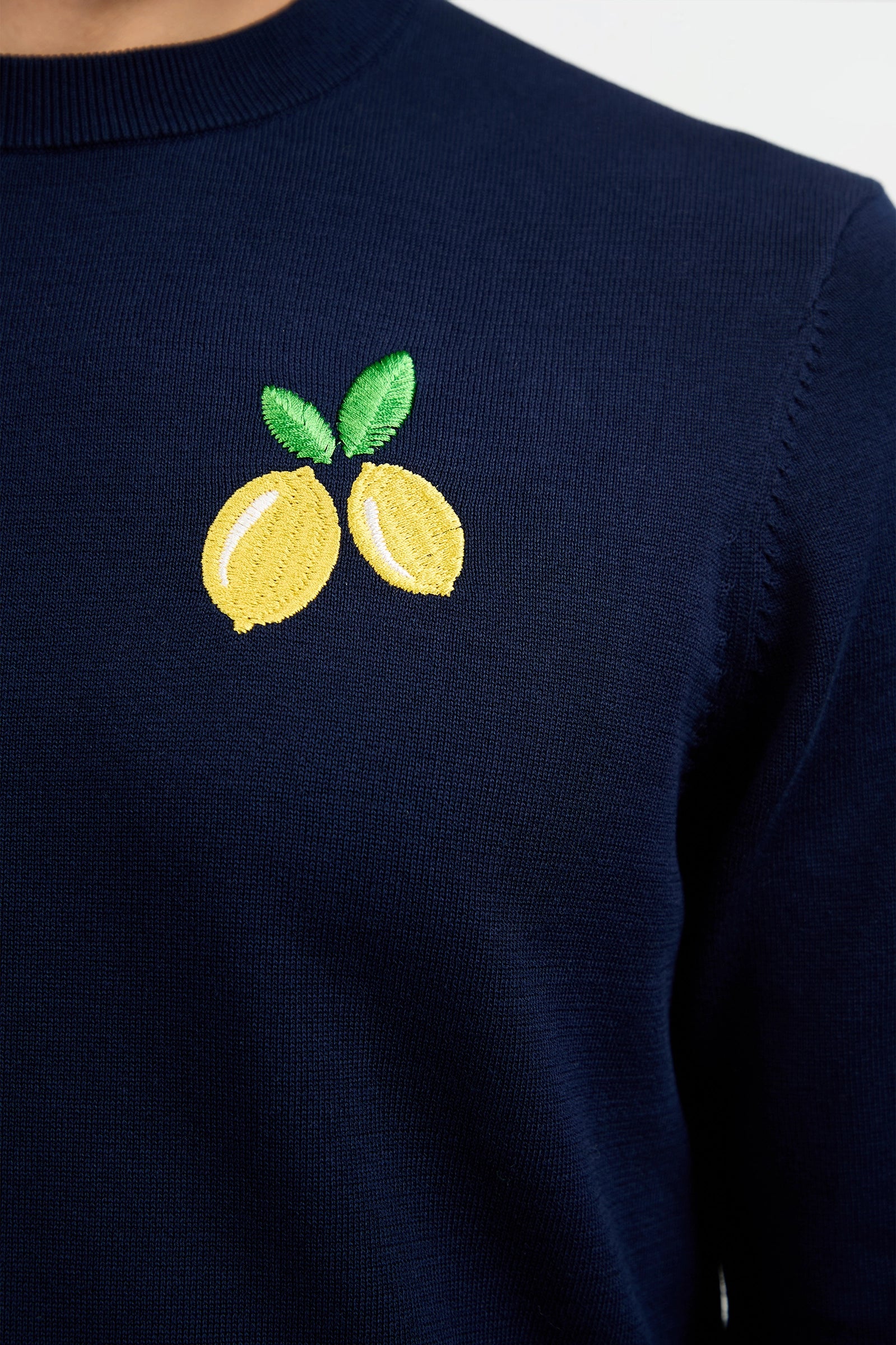 Close-up of the Meyer Long-Sleeve Crewneck Sweater in navy blue, featuring an embroidered design of two yellow lemons with green leaves on the upper chest.