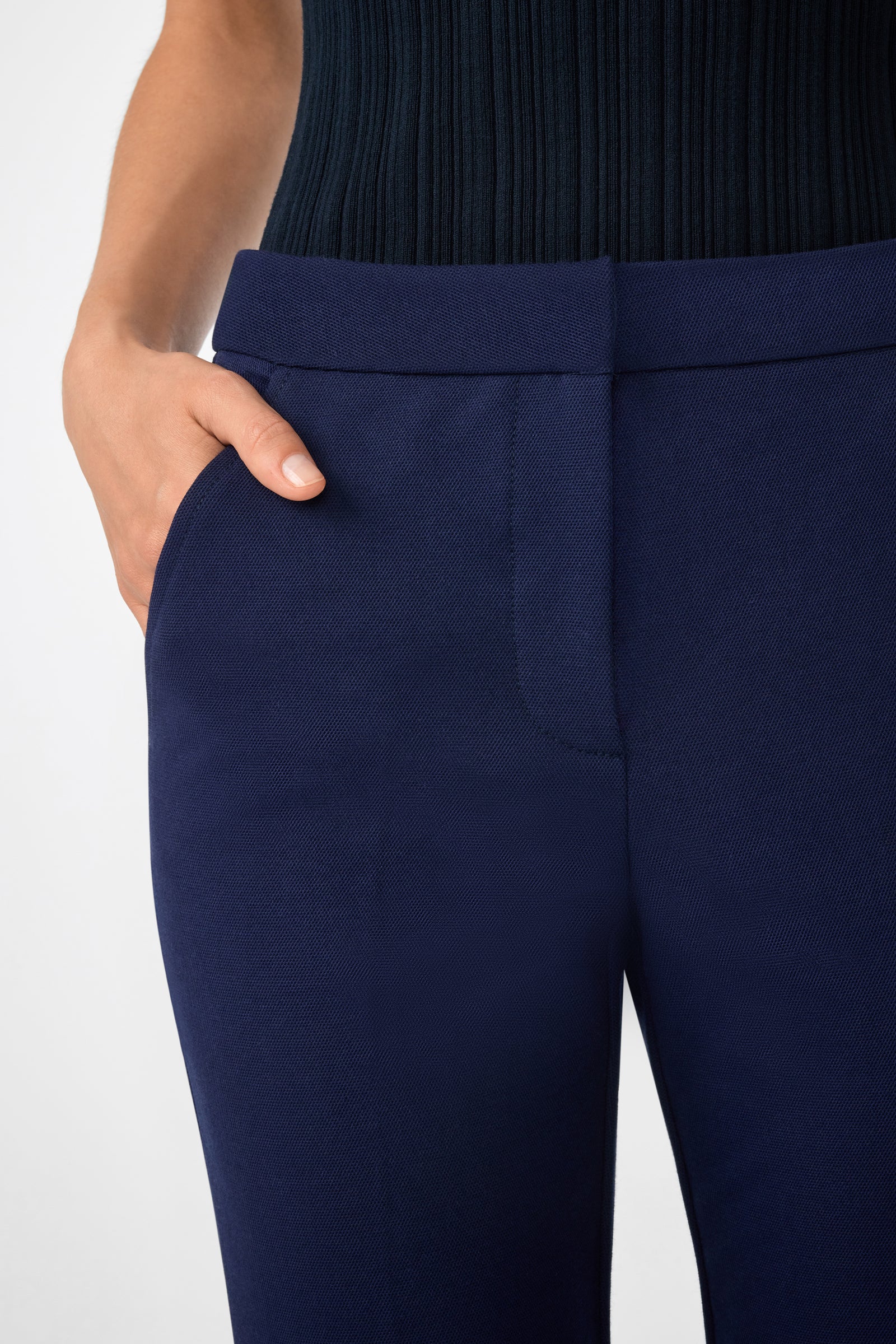 A person wearing the Banshee Pant in dark blue with one hand in their pocket, paired with a black ribbed top, shown from the waist down against a plain background.