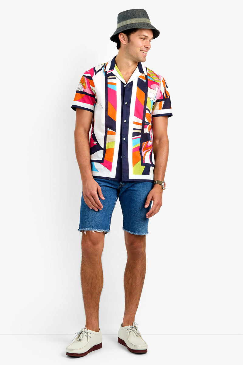 A man wearing the JOSUE CAMP SHIRT in MULTI, blue denim shorts, a gray hat, white shoes, and a wristwatch stands against a white background, smiling and looking to the side.