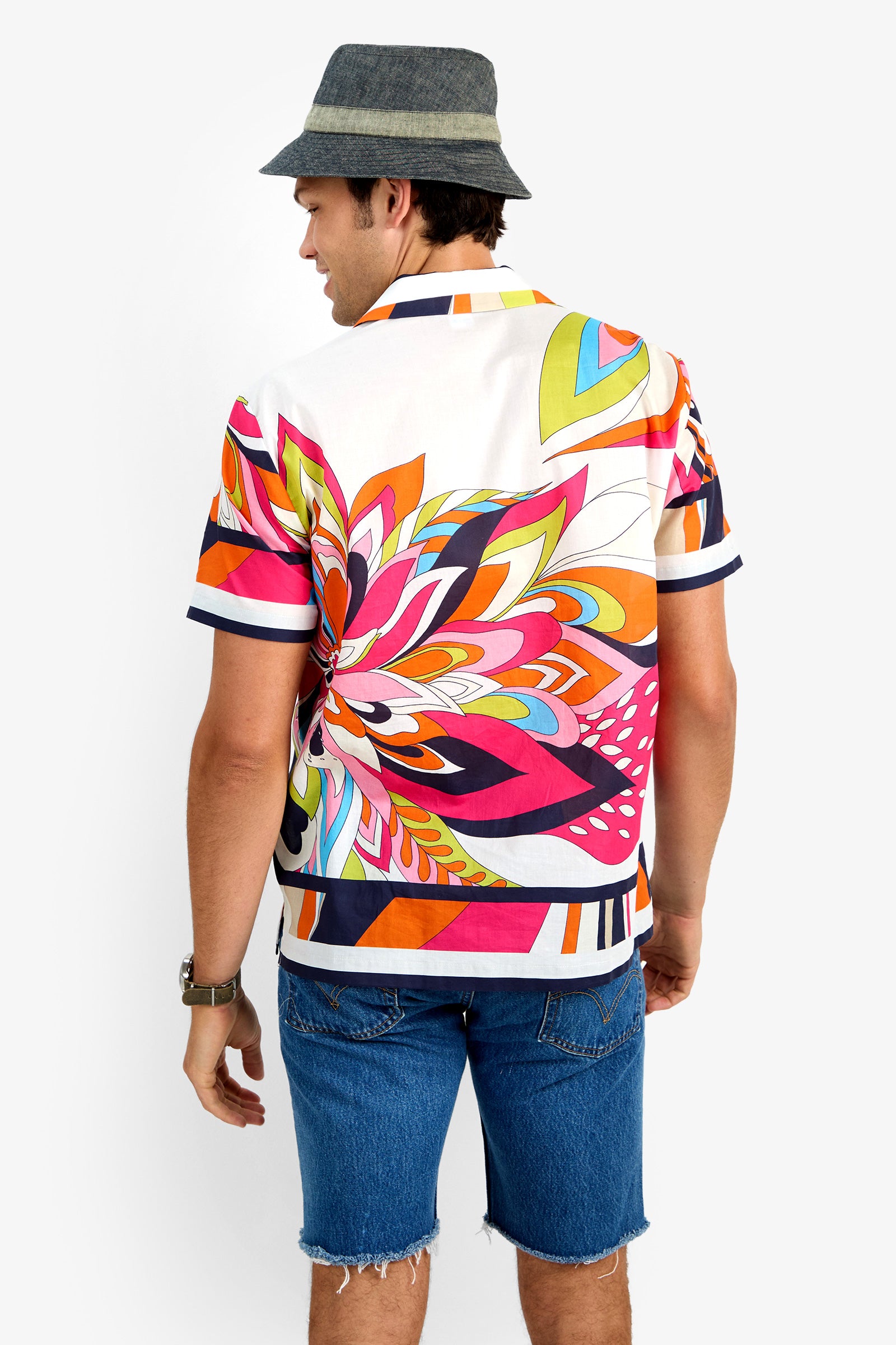 A man in the JOSUE CAMP SHIRT—an abstract-patterned, 100% cotton short-sleeve shirt—paired with denim shorts, a gray hat, and a watch stands facing away from the camera against a plain white background.