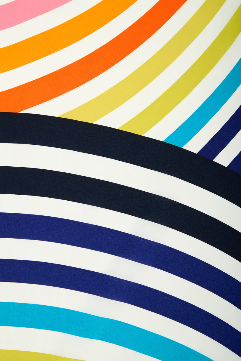 The Circle Scarf features an abstract, vibrant pattern of curved stripes in bright colors such as pink, orange, yellow, green, blue, black, and white.