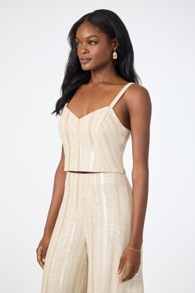 A woman with long dark hair wearing gold earrings and the Millau Sleeveless Top with matching wide-leg pants stands against a plain light background.